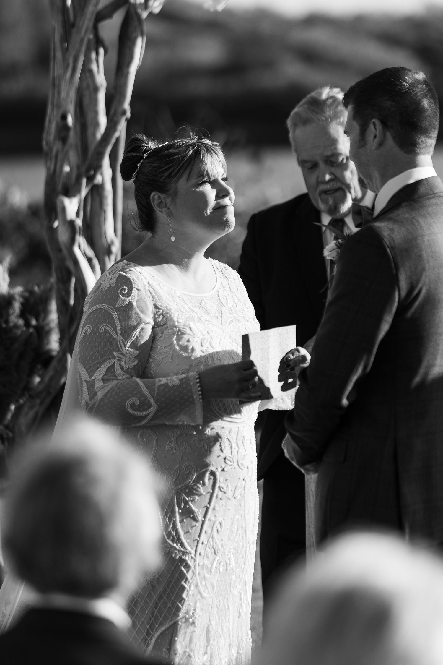 Black and white photo of bride reading vows to groom at outdoor wedding ceremony.