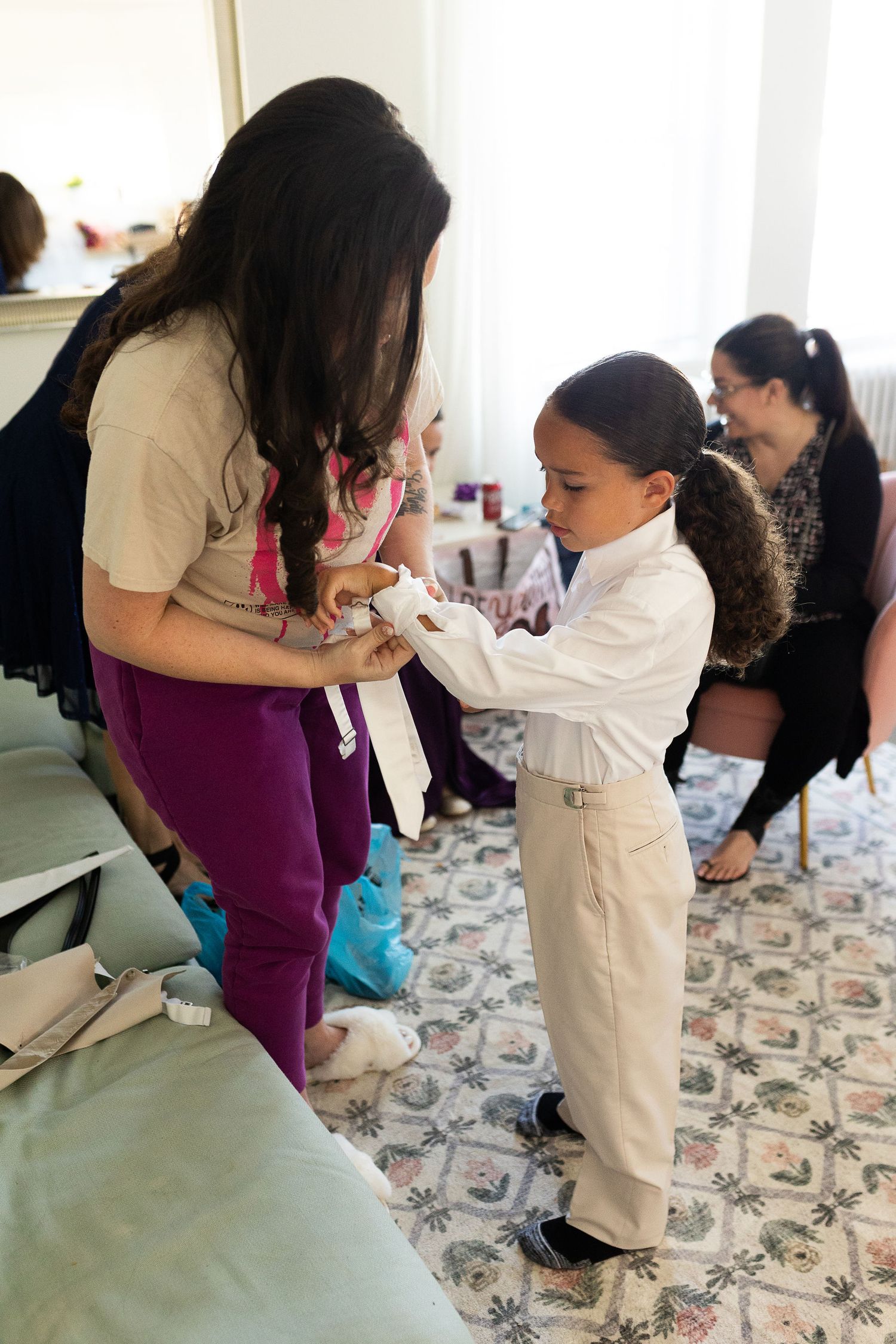 Woman helping young boy in white shirt adjust his outfit before a wedding ceremony.