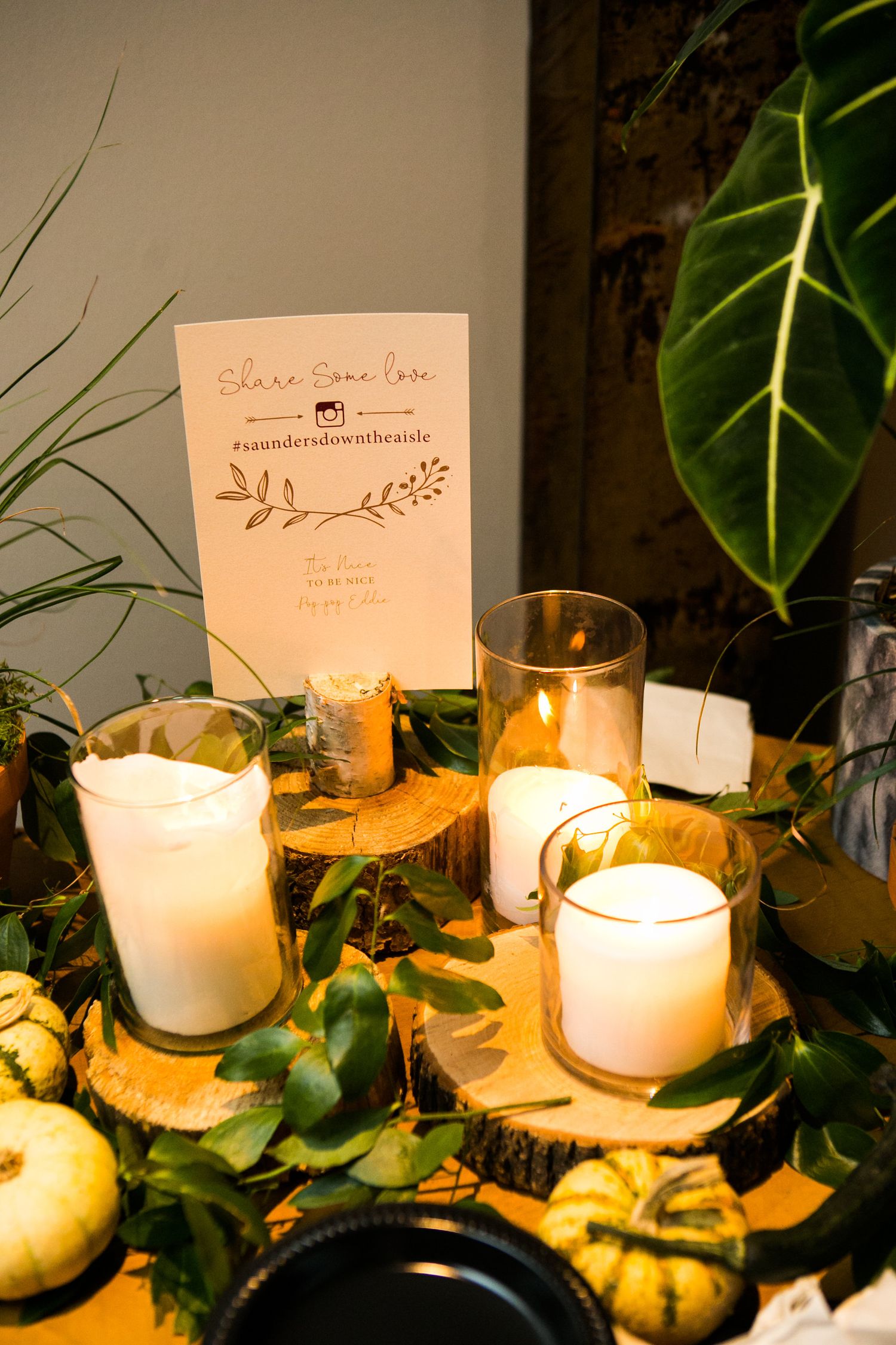Wedding decor display with candles, greenery, pumpkins, and social media hashtag sign.