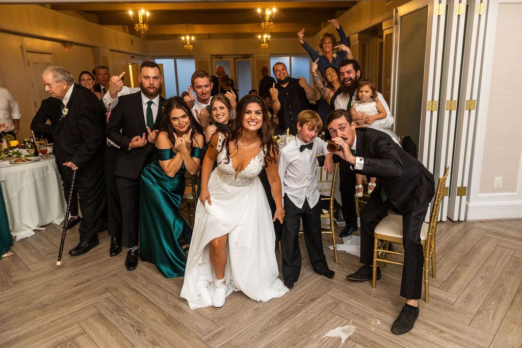 Bride and groom pose with wedding guests in a festive group photo at an elegant indoor reception venue.