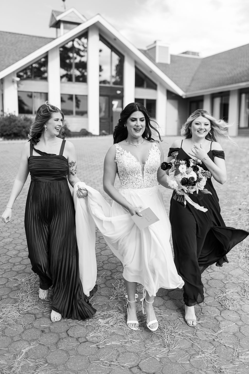 Black and white photo of a bride and two bridesmaids walking confidently outside a wedding venue on a windy day.