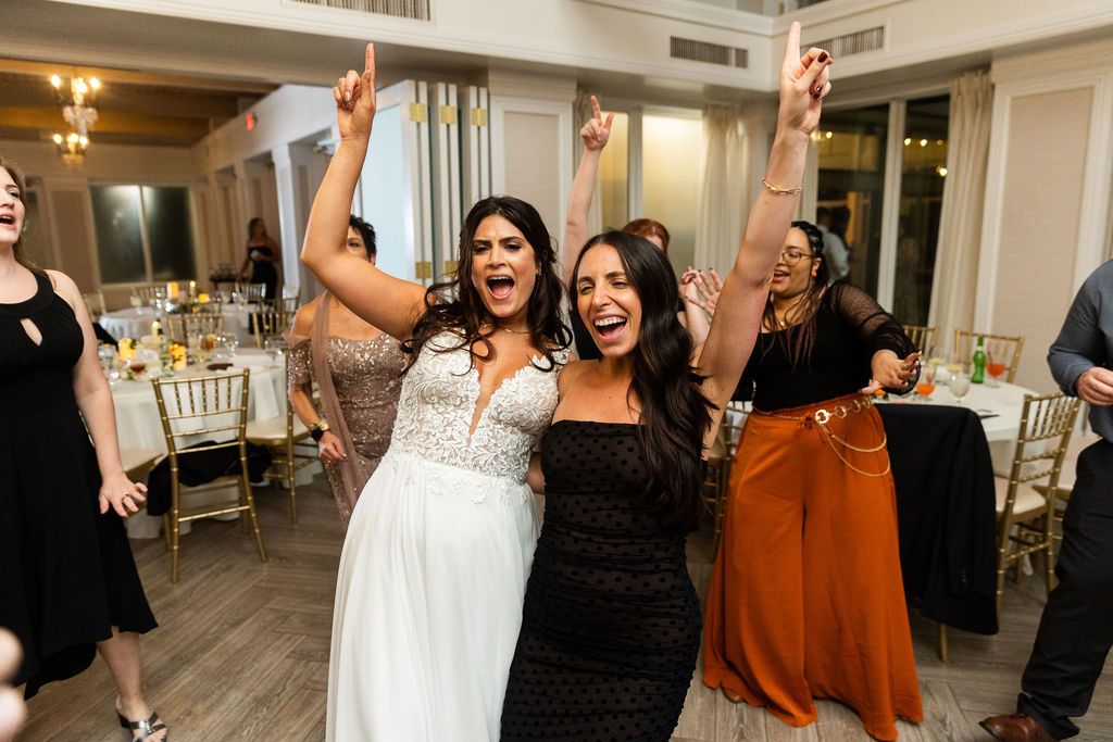 Bride and friend celebrating with arms raised at colorful wedding reception party.