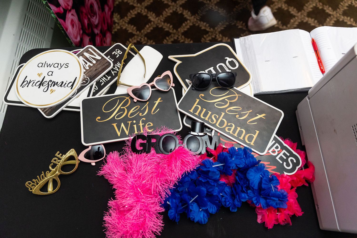 Wedding photo booth props including Best Wife, Best Husband, and Groom signs on black table.