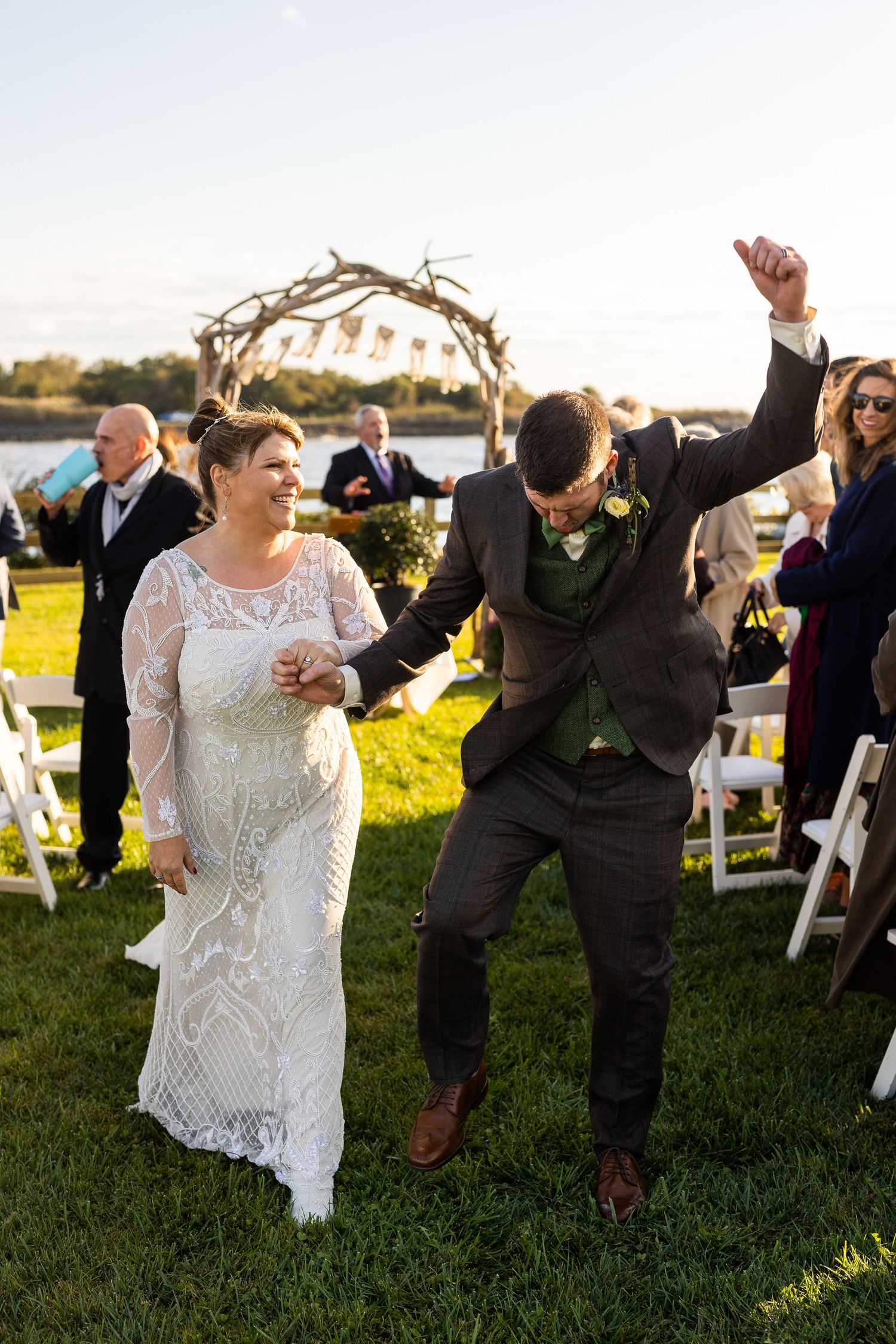 Jubilant groom pumping fist in air while walking down aisle with bride after wedding ceremony.