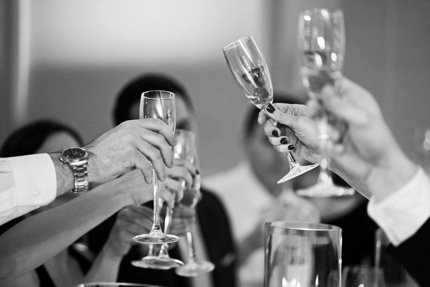 Wedding guests raising champagne glasses in a celebratory toast in black and white photo.