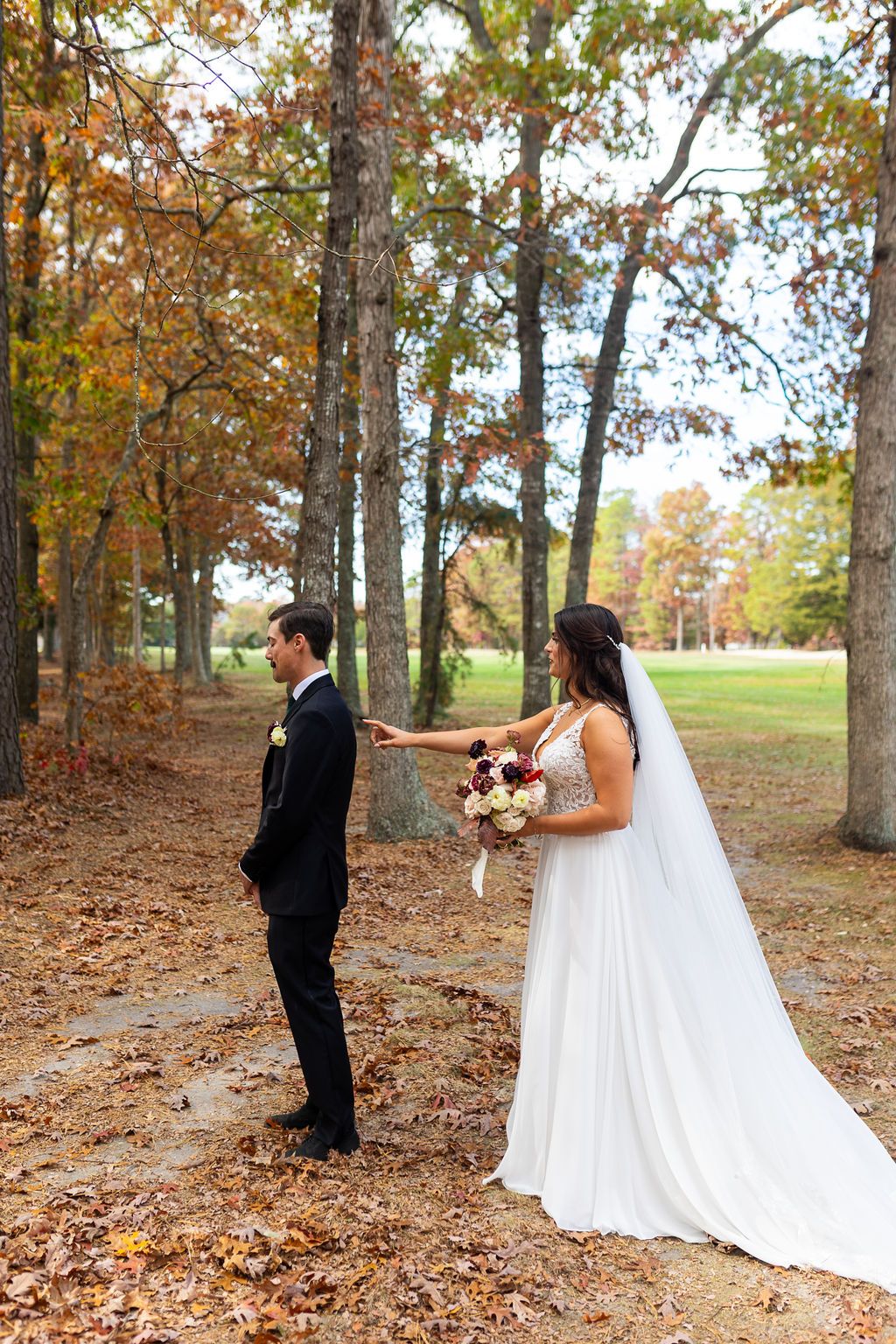 Bride tapping groom on the shoulder for their first look among autumn foliage in an outdoor wooded setting.
