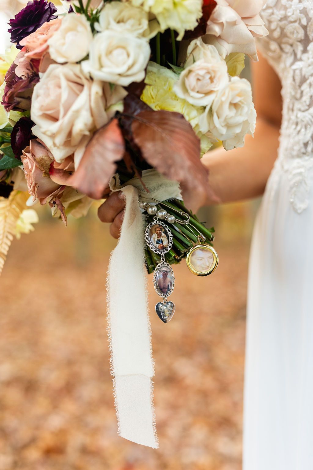 Bride holding autumn wedding bouquet with roses and memorial charms on ribbon.