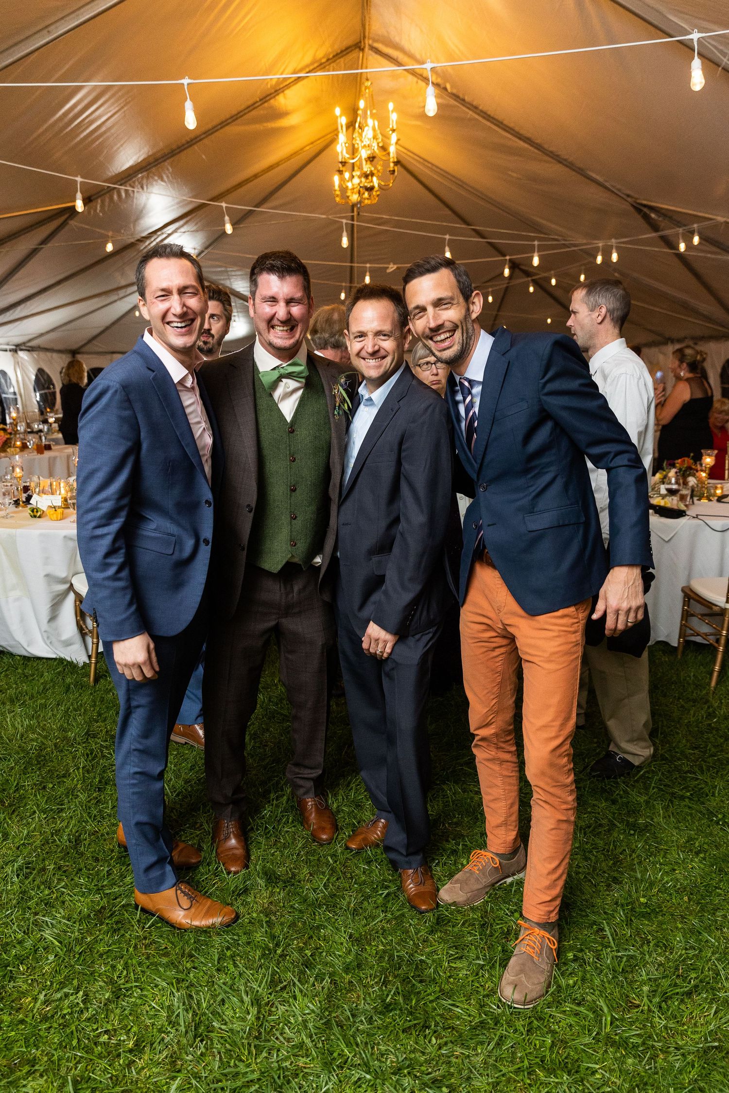 Four men in suits smiling and posing together at an elegant outdoor wedding reception.