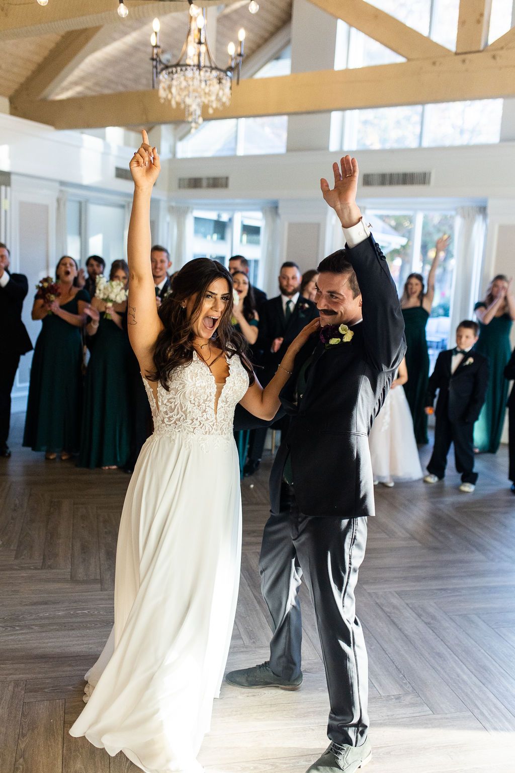 Excited bride and groom raise arms in celebration during grand entrance at wedding reception.