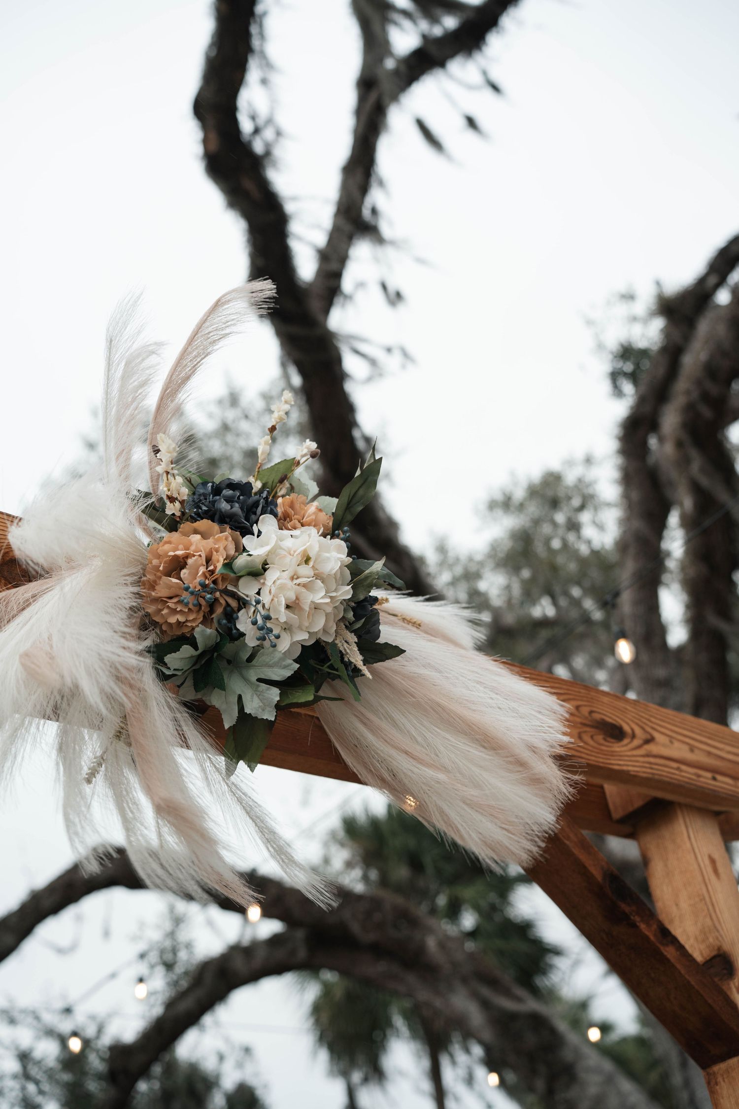Rustic wooden wedding arch decorated with pampas grass and peach floral arrangement.