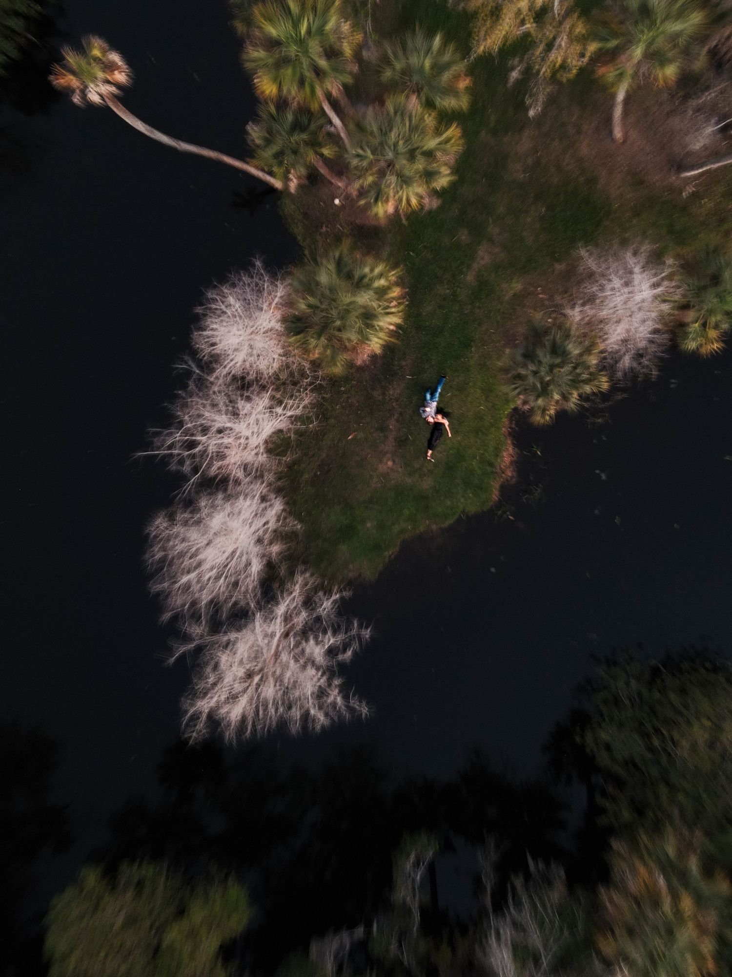 Aerial drone view of a person lying on a green island surrounded by dark water.