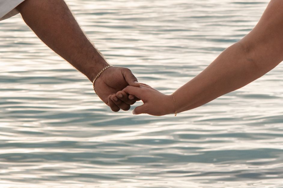 Newlywed couple holding hands near ocean water after beach wedding ceremony.