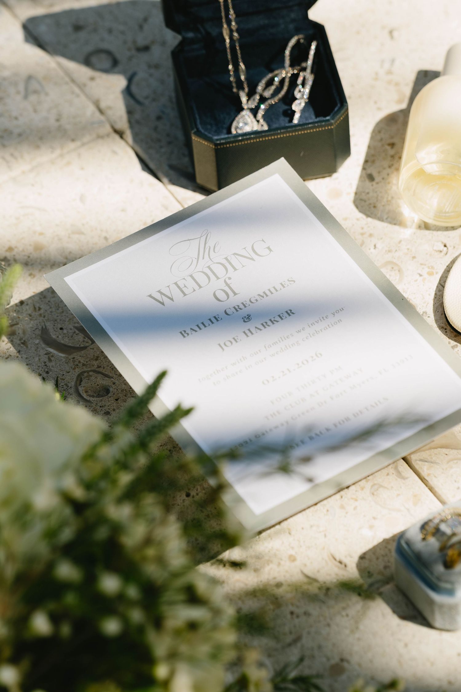 Wedding invitation for Bailie Creighley and Joe Harker displayed with diamond jewelry and a candle.