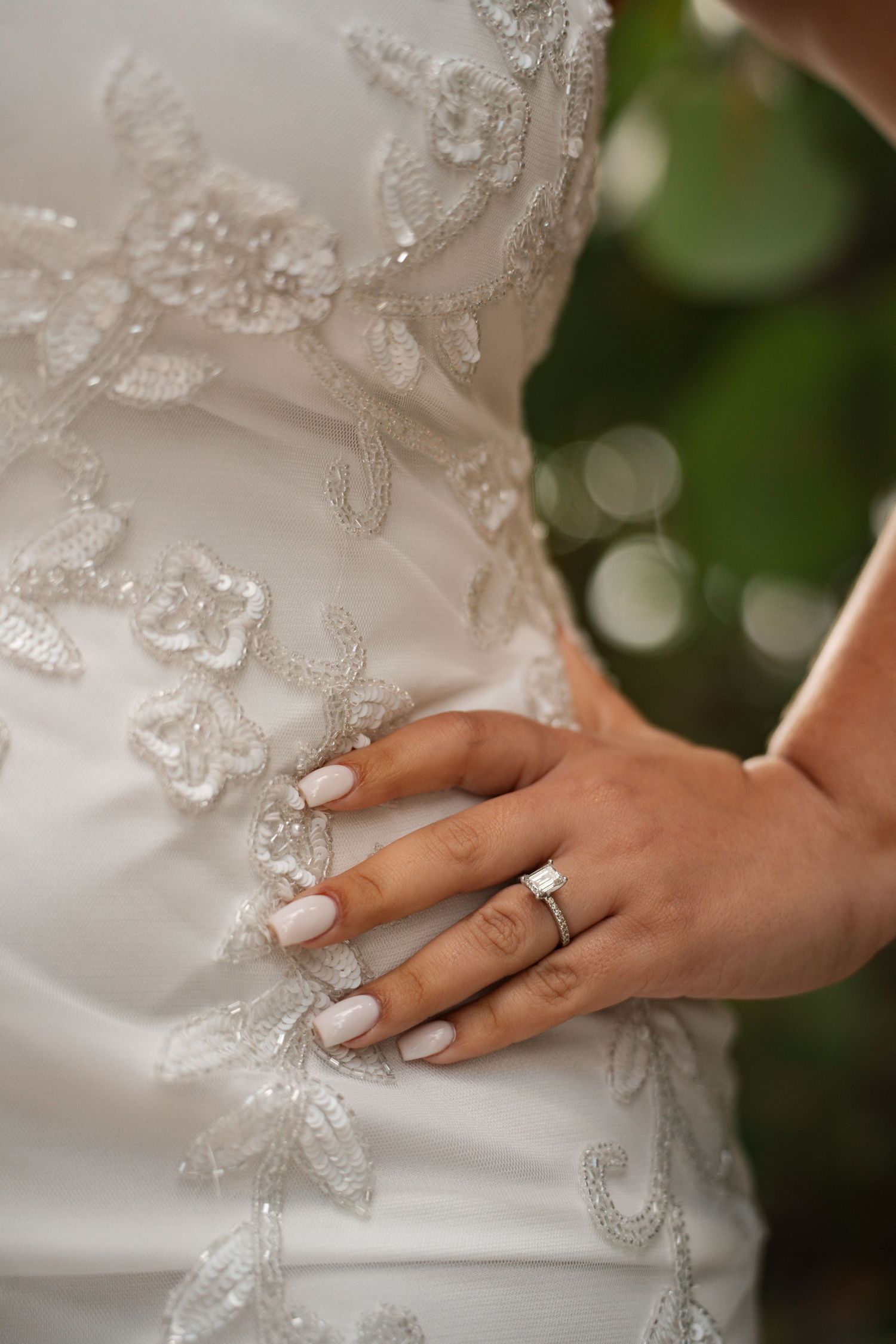 Close-up of bride's hand with diamond engagement ring on lace wedding dress.