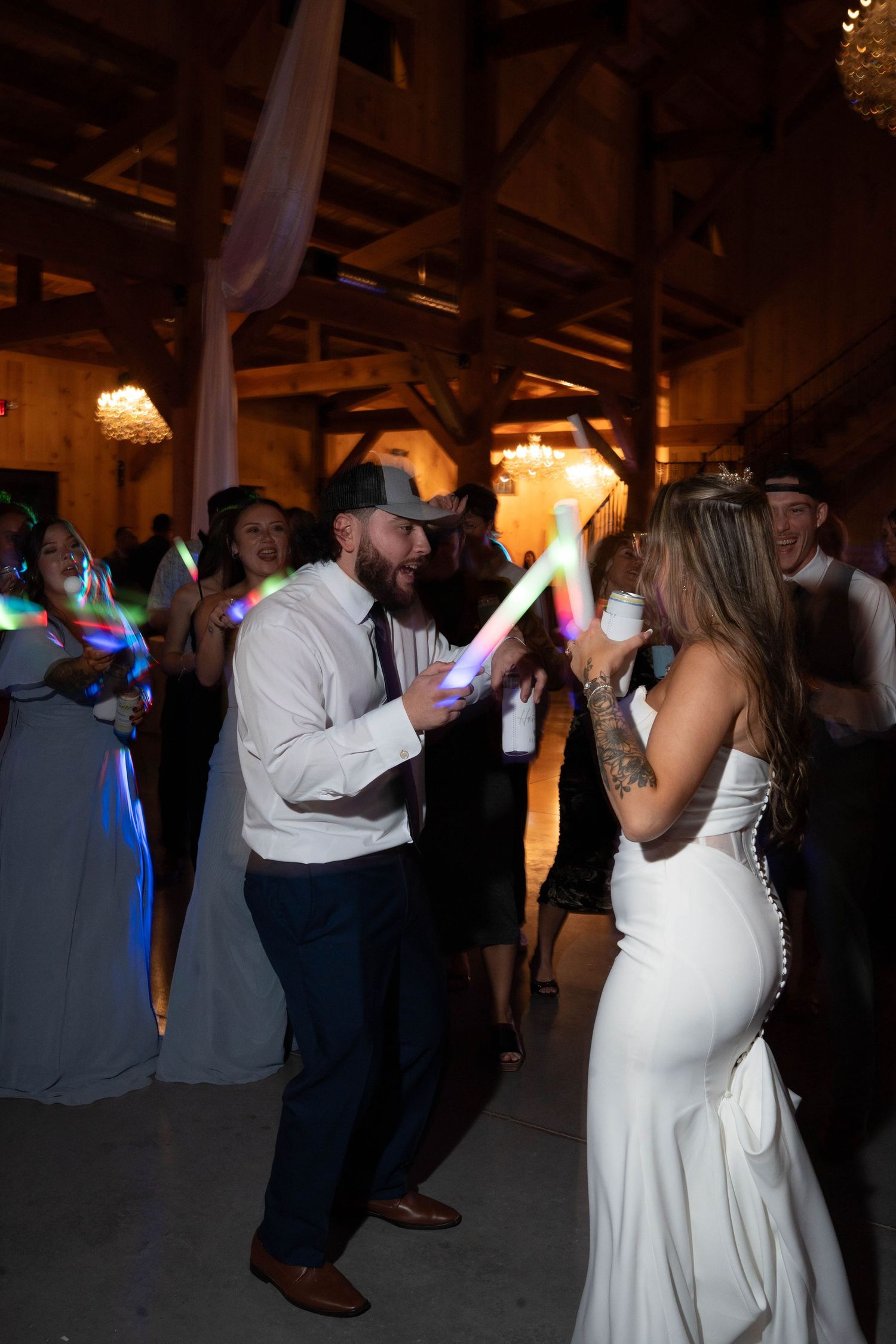 Bride and guest dance together with colorful LED foam sticks at wedding reception.