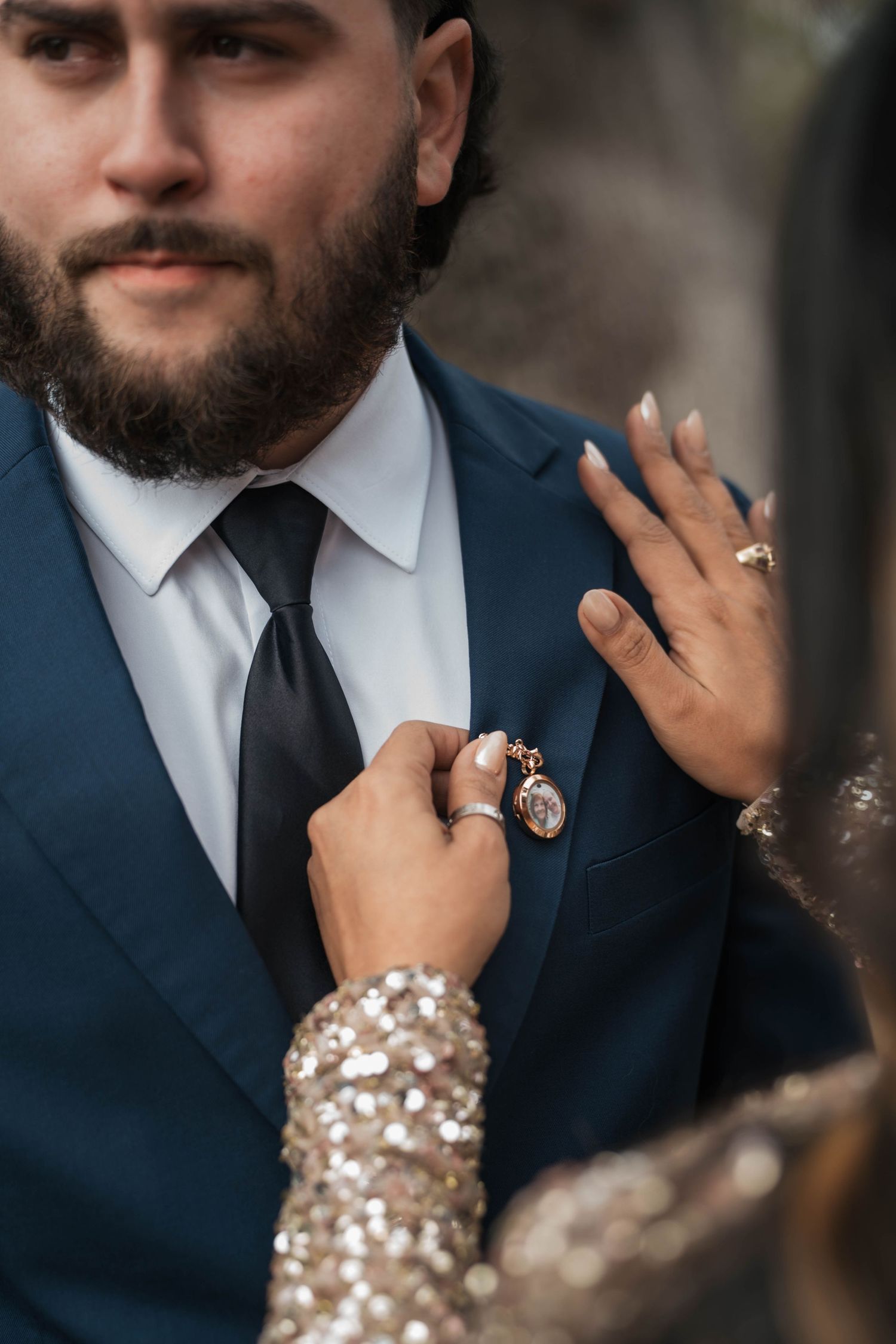 Bride adjusts rose gold locket boutonniere on groom's navy suit lapel.
