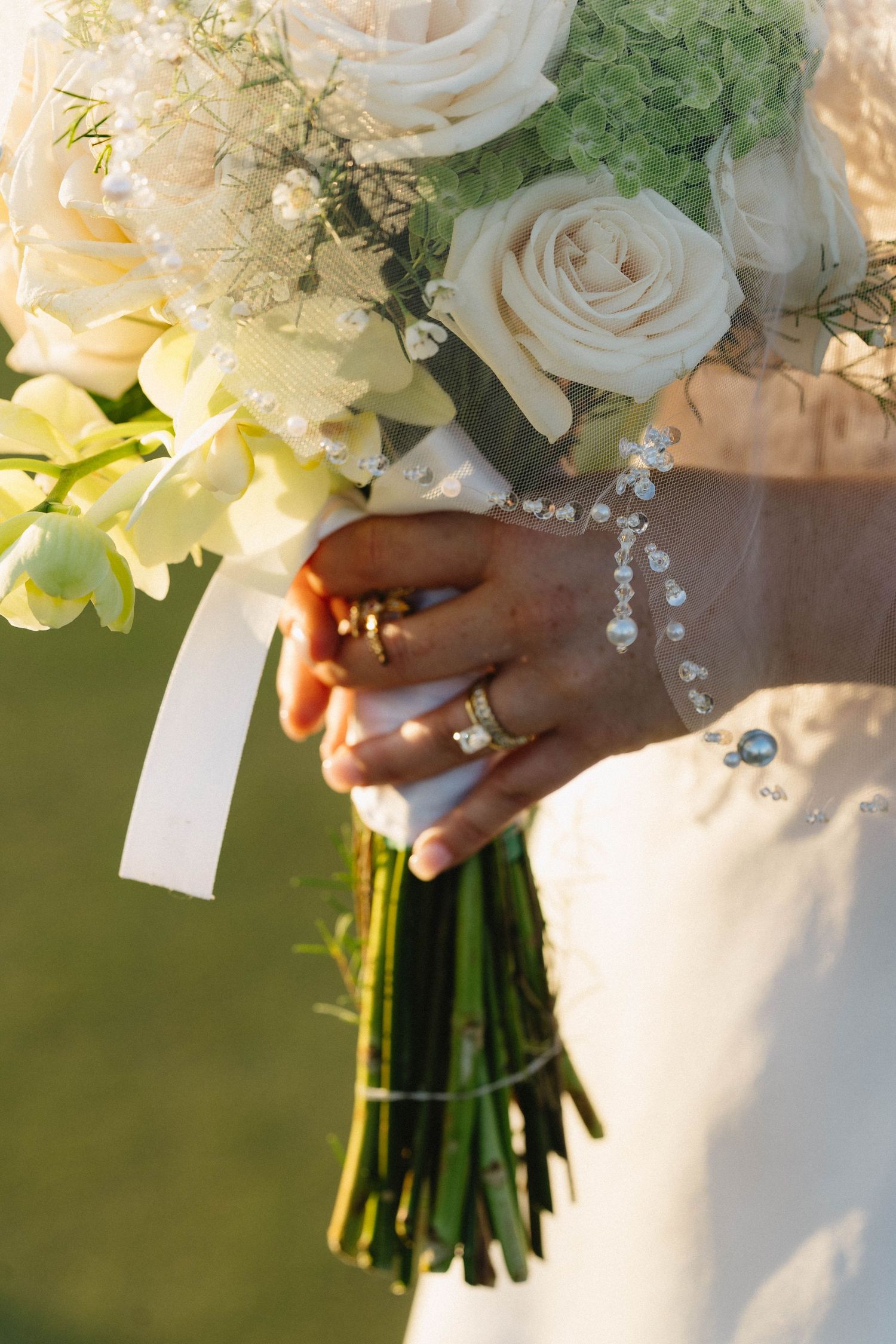 Close-up of bride holding white rose wedding bouquet with diamond ring and bracelet.