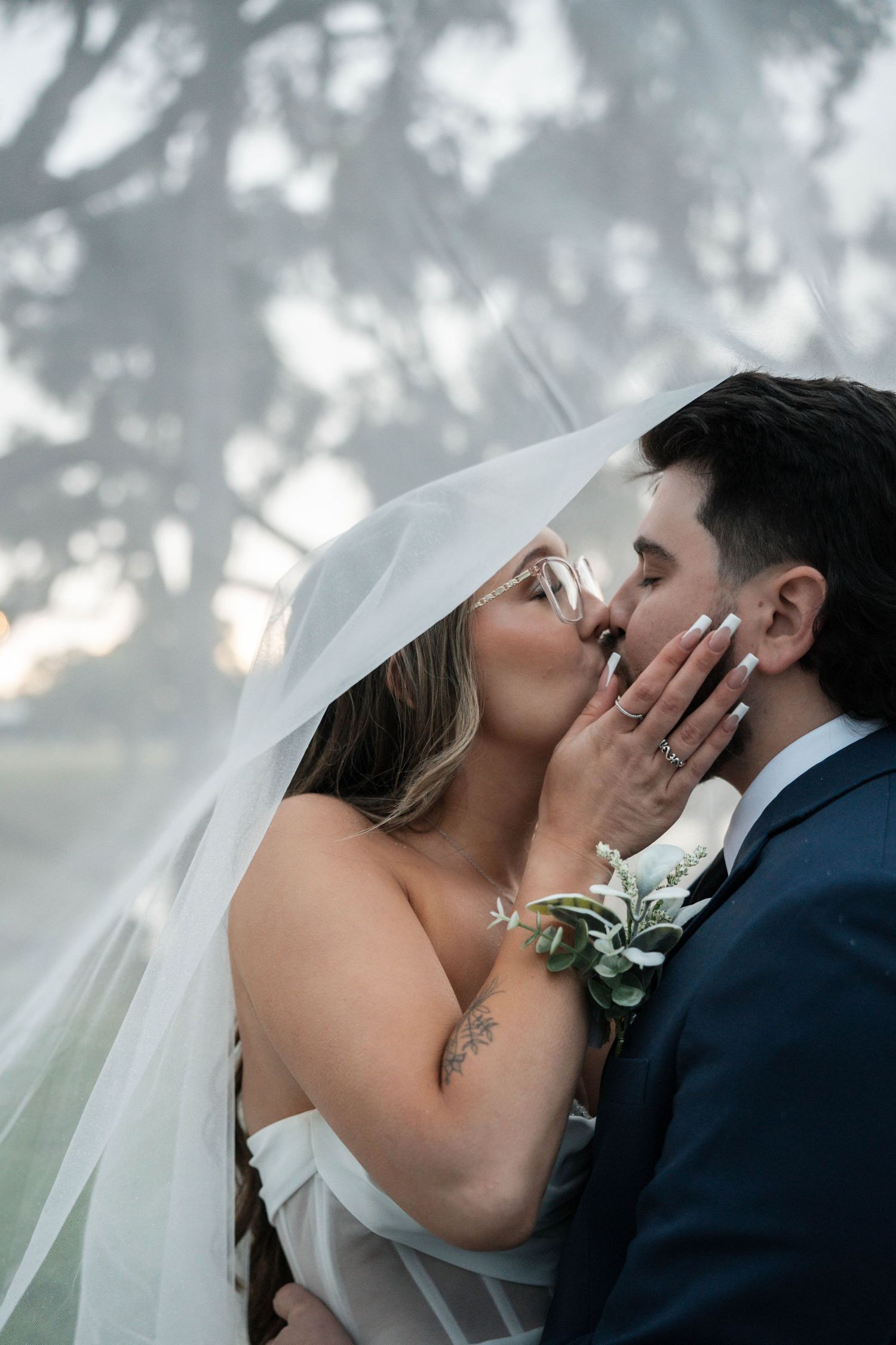 Bride and groom share a passionate kiss under flowing wedding veil at outdoor ceremony.