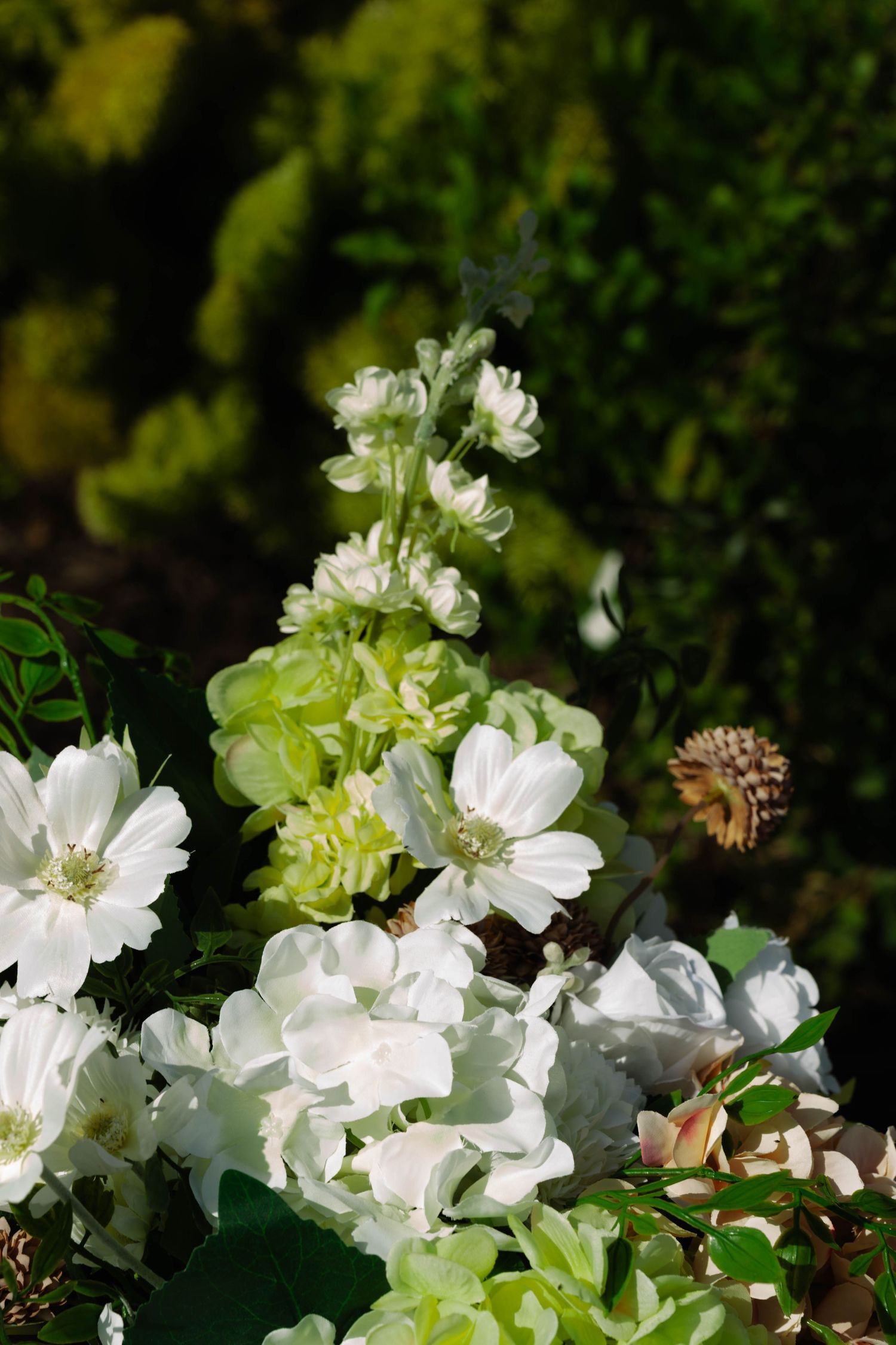 White hydrangea and delphinium wedding floral arrangement against a lush dark green garden backdrop.