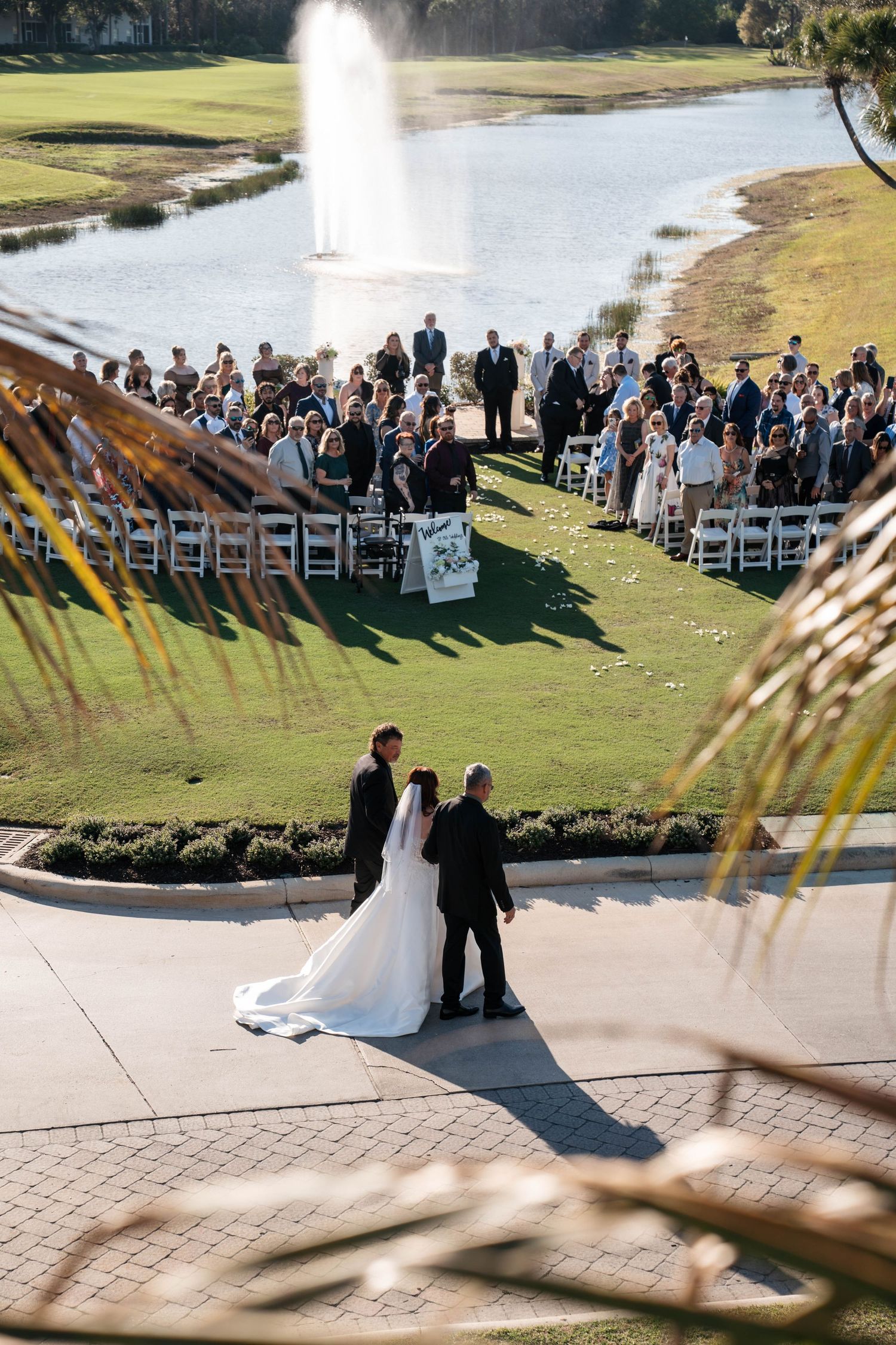 Aerial view of outdoor wedding ceremony on golf course with fountain and seated guests.