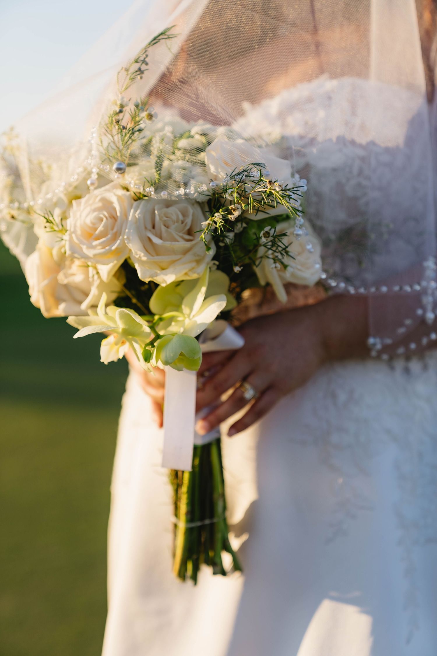 Bride holding an elegant white rose and green hydrangea wedding bouquet tied with a white ribbon.