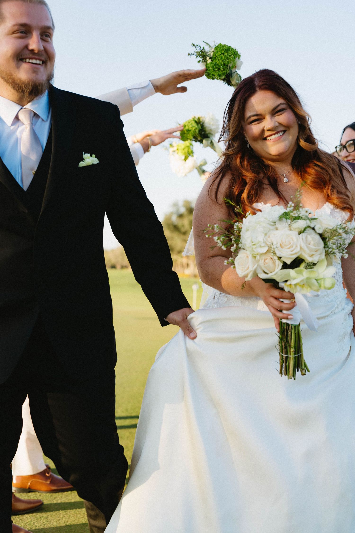 Laughing bride and groom walking hand in hand during joyful outdoor wedding celebration.