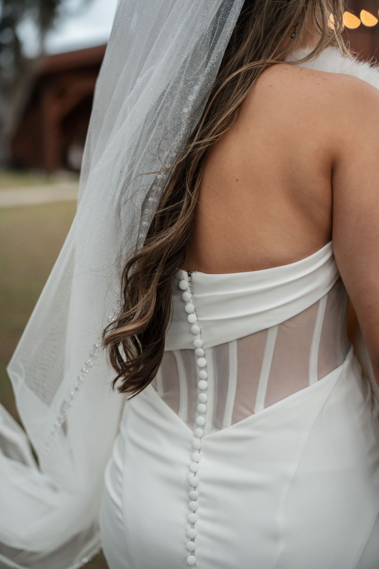 Close-up detail of brides corset back wedding gown with pearl buttons and sheer panel under veil.