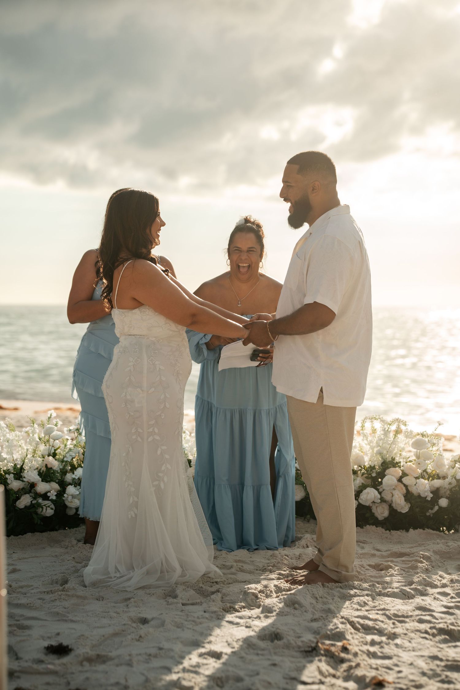Bride and groom holding hands during sunset beach wedding ceremony with officiant.