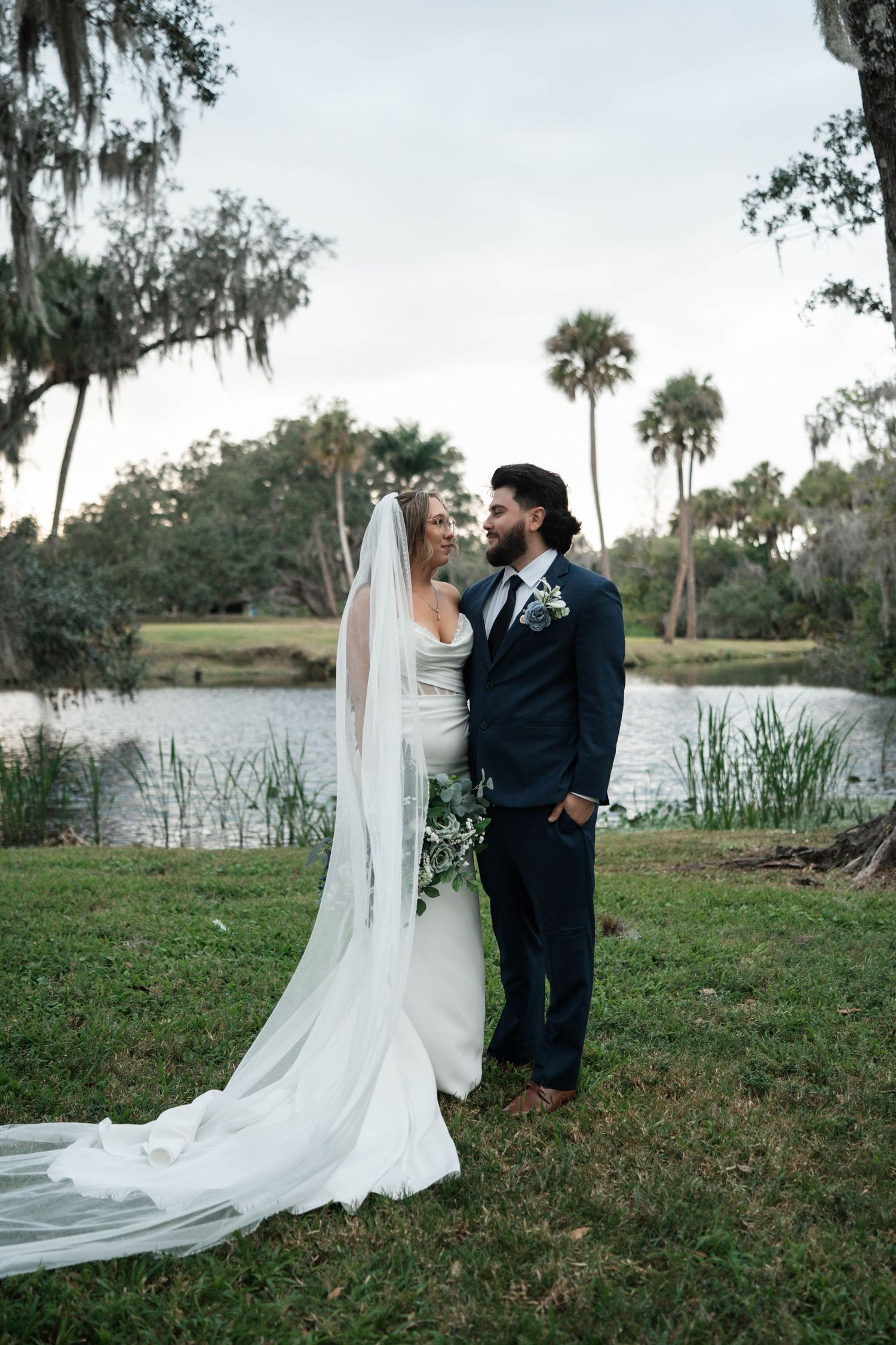 Wedding couple poses romantically by a serene pond surrounded by Spanish moss-draped trees in Florida.