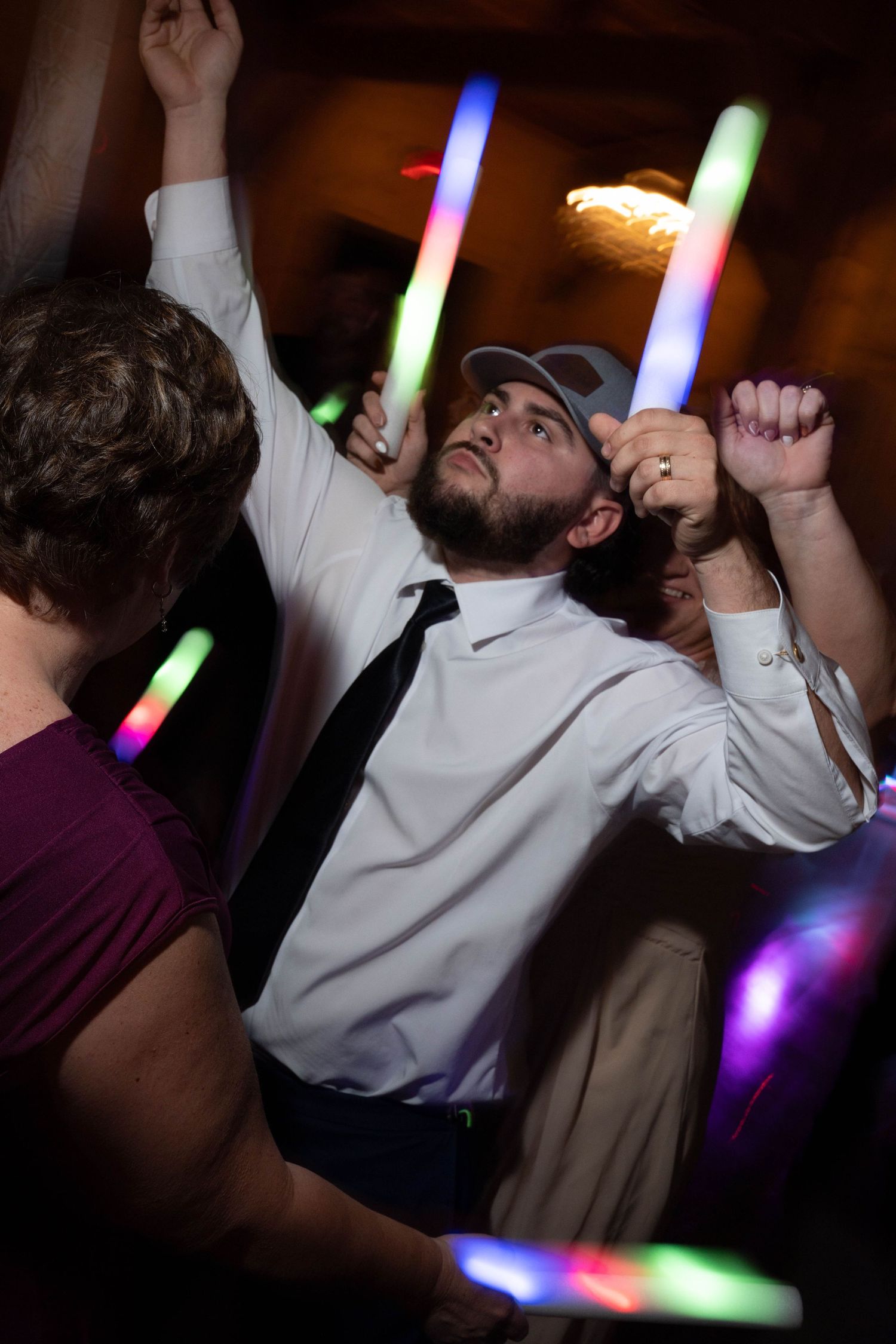 Wedding guest dances energetically with colorful glow sticks at lively reception.
