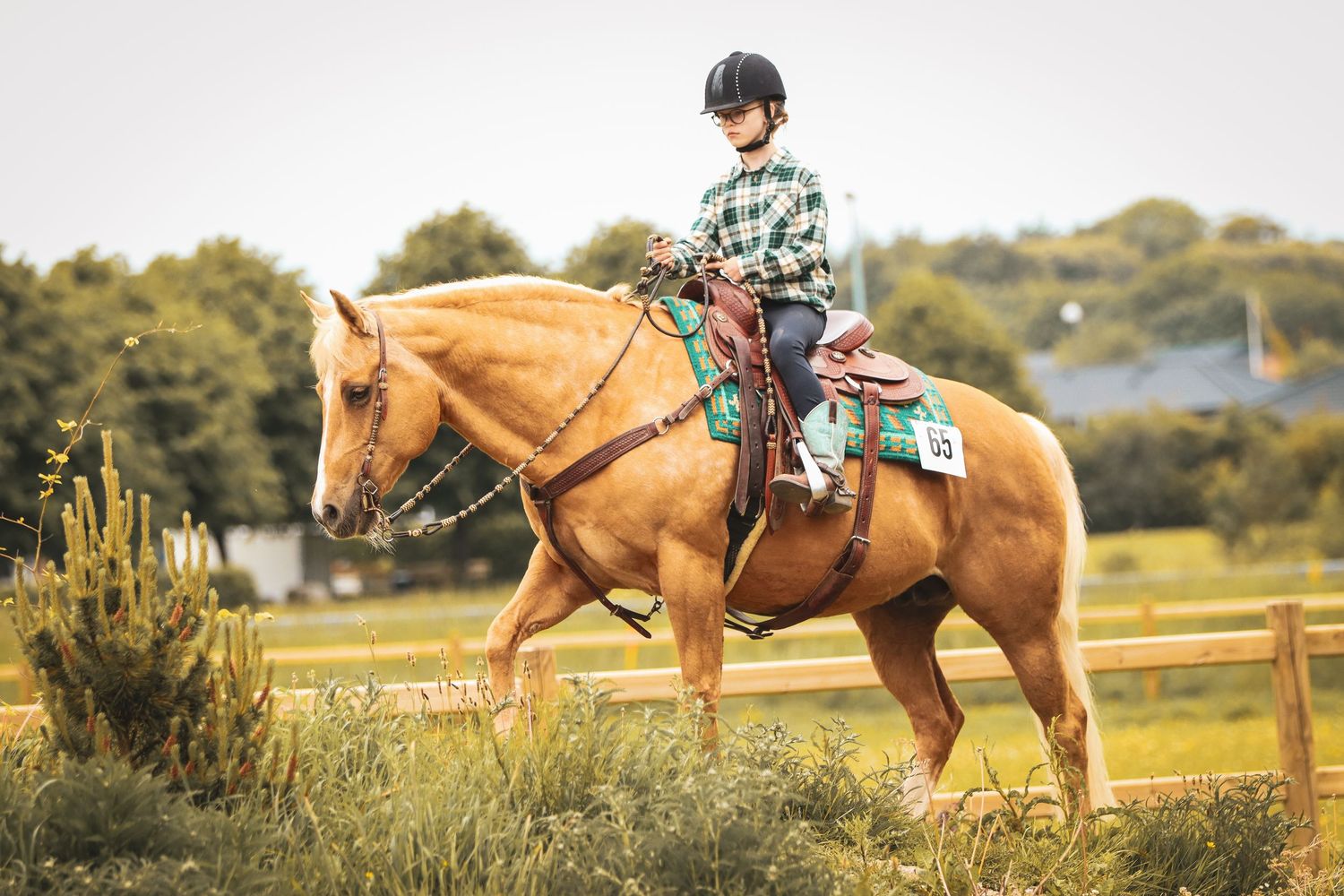 Young rider on a palomino horse competing in an outdoor Western equestrian show event.