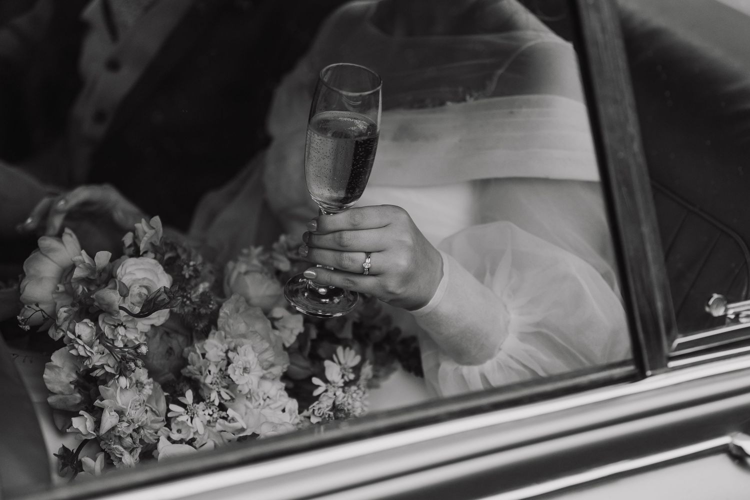 Black and white prosecco glass close up held by woman's hand with wedding and engagement ring