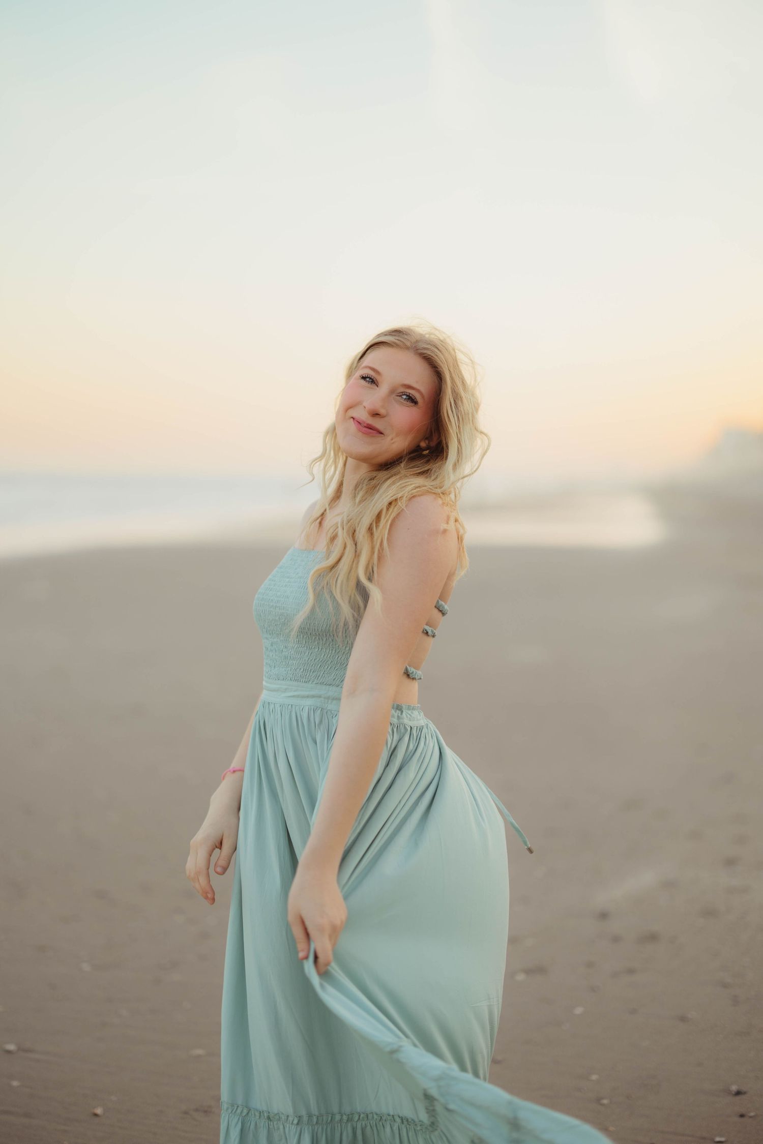A blonde woman in a flowing mint green dress stands on a beach at sunset. Lafayette indiana tippecanoe county west lafayette
