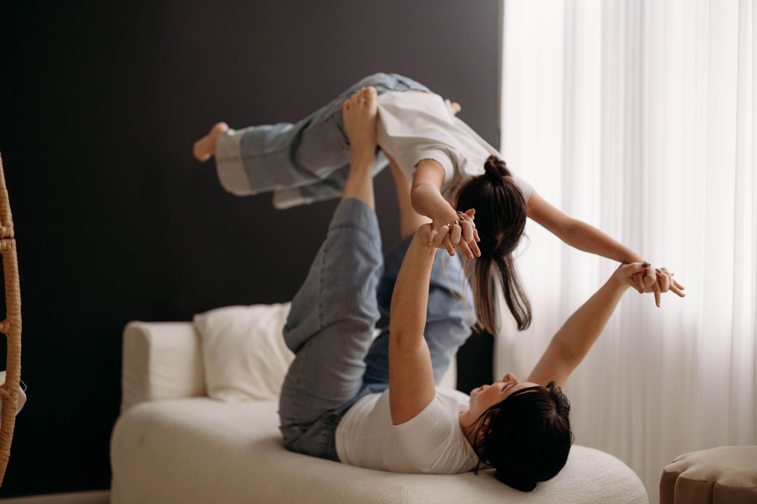 Parent lying on sofa playfully lifting child in the air near a bright window. Lafayette indiana tippecanoe county west lafayette