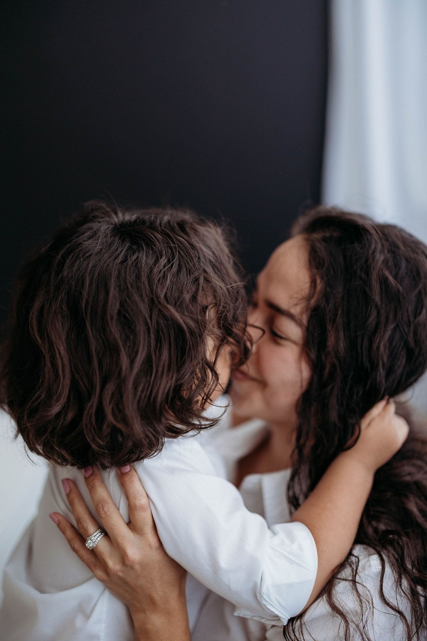 A mother with dark curly hair kisses her young child tenderly while embracing them in a warm hug. Lafayette indiana tippecanoe county