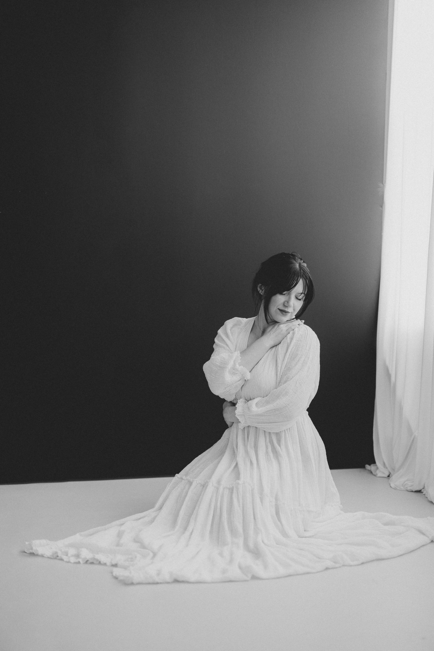 Black and white portrait of woman in white robe kneeling on studio floor looking down. Lafayette indiana tippecanoe county west lafayette