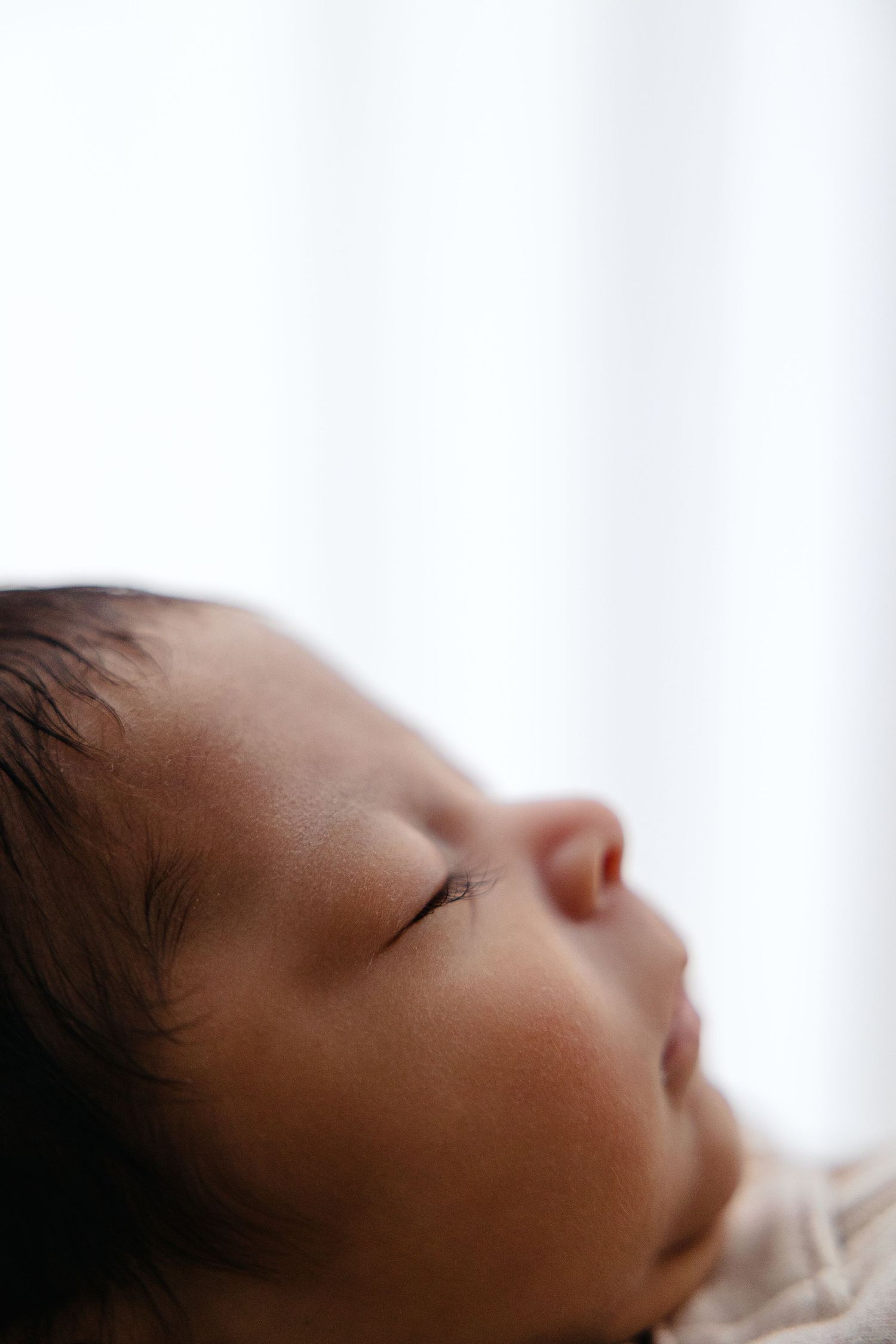 Serene close-up side profile of sleeping newborn baby with dark hair against bright white backdrop. Lafayette indiana tippecanoe county