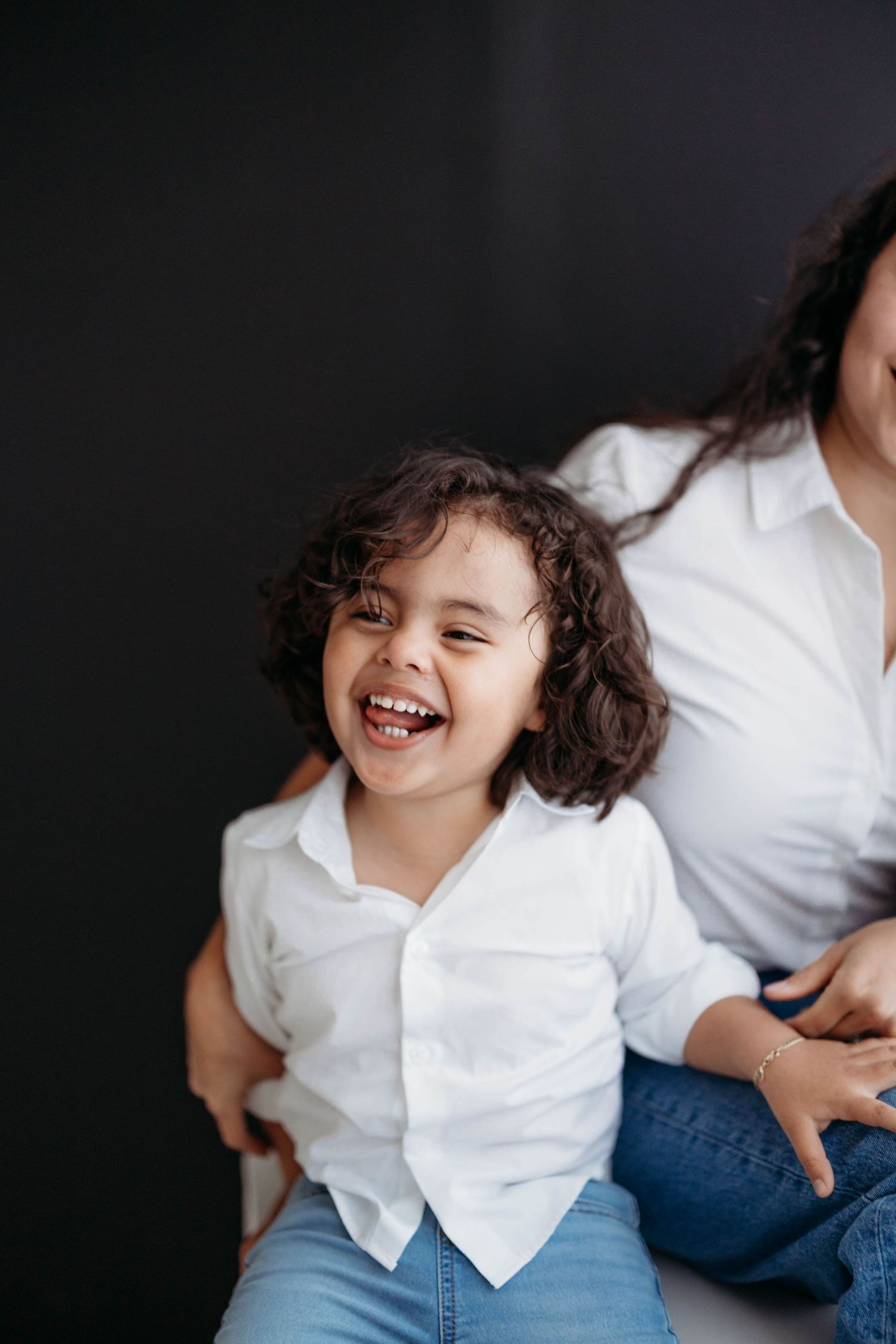 A joyful young child with curly hair laughs brightly while sitting with their mother in white shirts. Lafayette indiana tippecanoe county