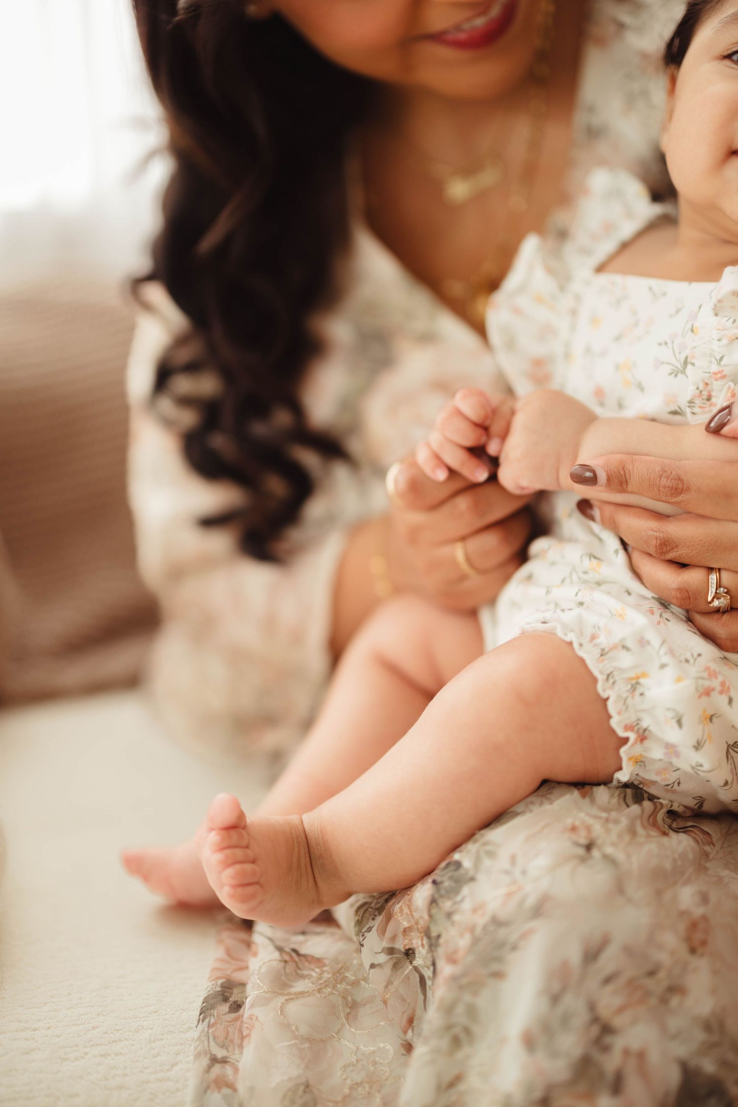 Mother in floral dress holding baby on lap while gently playing with tiny infant hands and feet. Lafayette indiana tippecanoe county