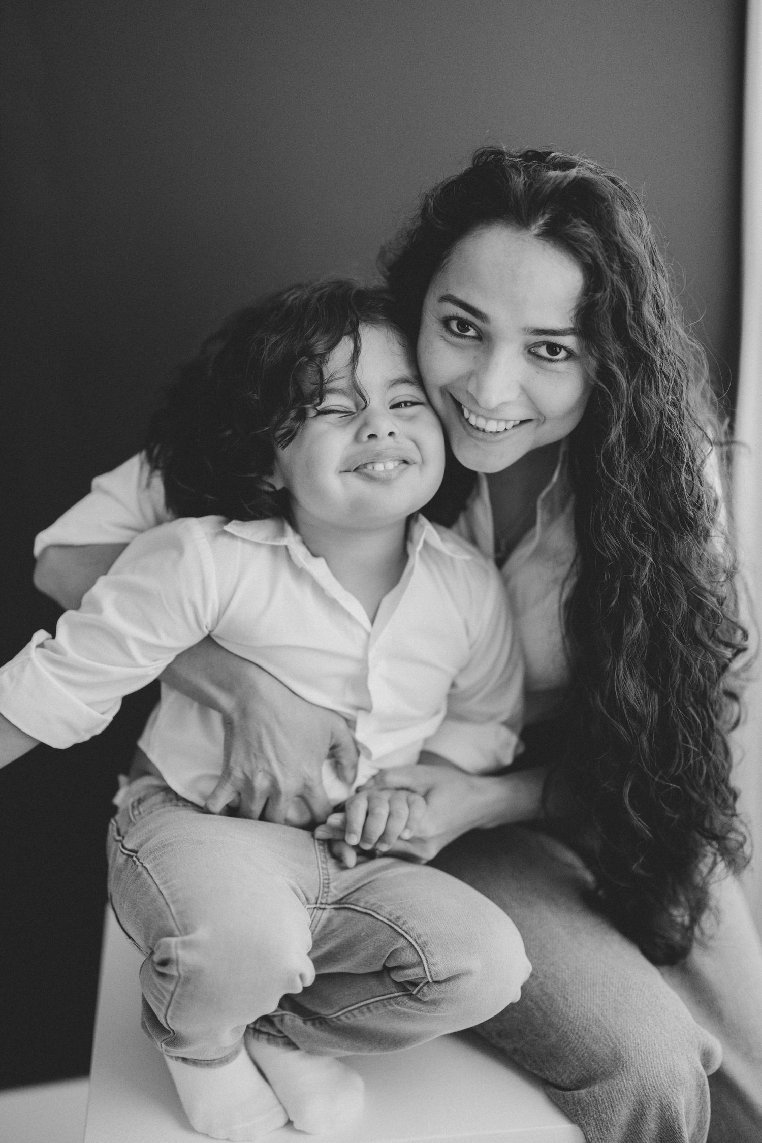 Black and white photo of a smiling mother with curly hair hugging her laughing young child. Lafayette indiana tippecanoe county