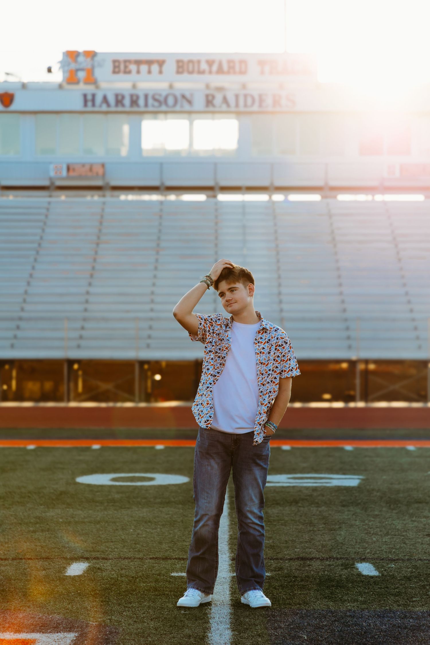 Teen boy in patterned shirt on a football field at Harrison Raiders stadium at sunset. High school senior photos in west Lafayette indiana