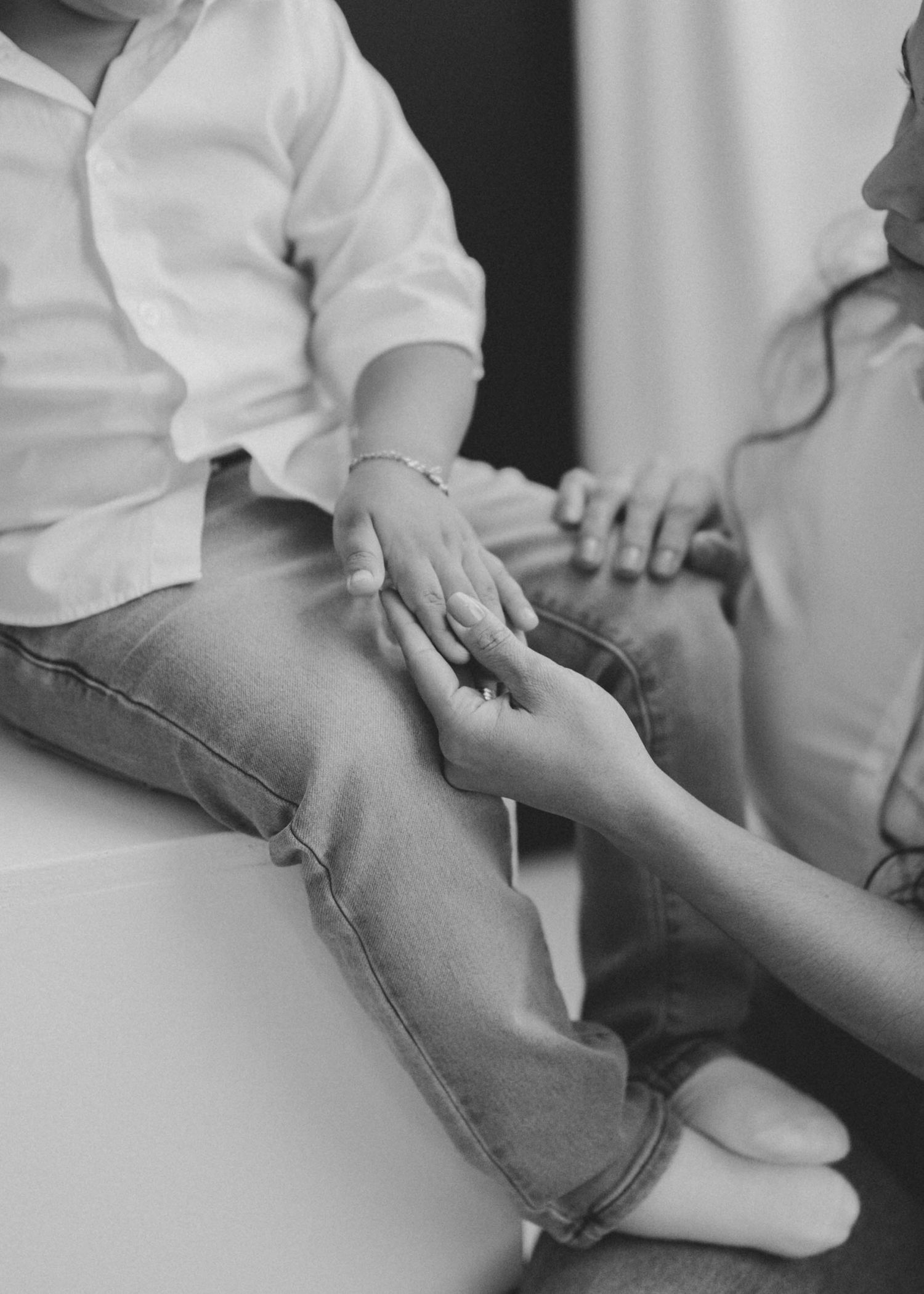 Black and white photo of an adult tenderly holding a young child's hands while sitting together indoors.