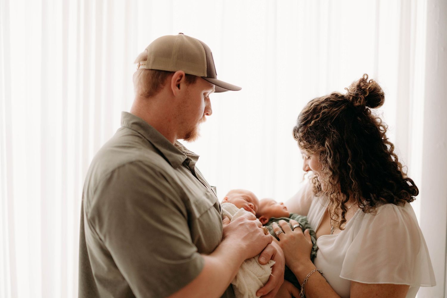 New parents in casual clothing tenderly hold their newborn baby together near bright white curtains. Lafayette indiana tippecanoe county