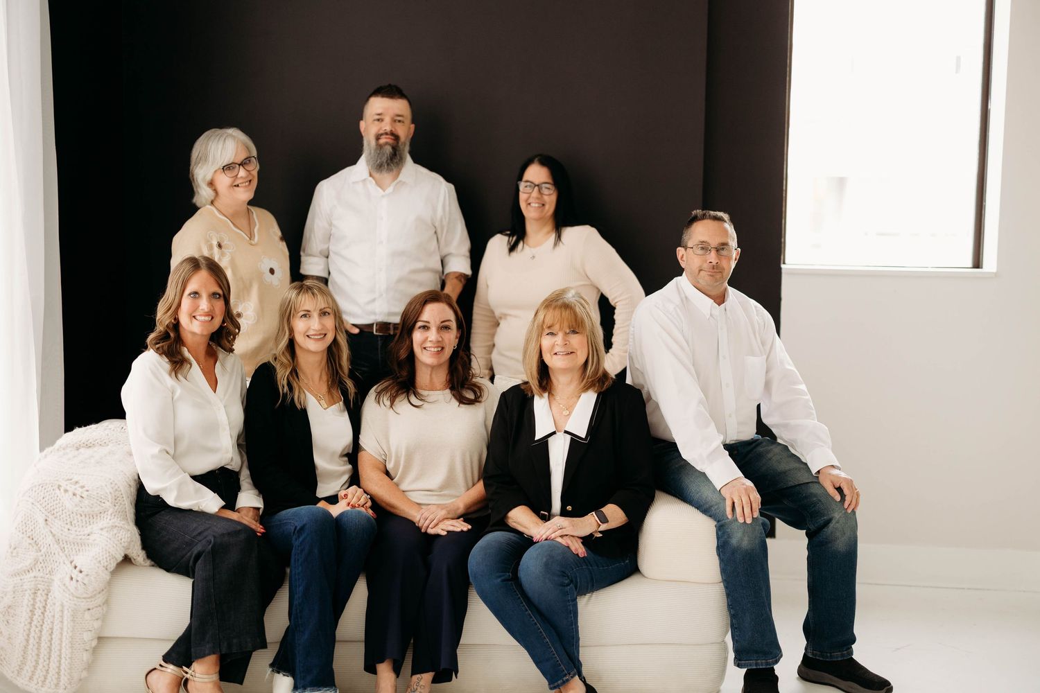 Group of nine professionals posing together on white couch in modern studio setting.Branding photos in west Lafayette Indiana