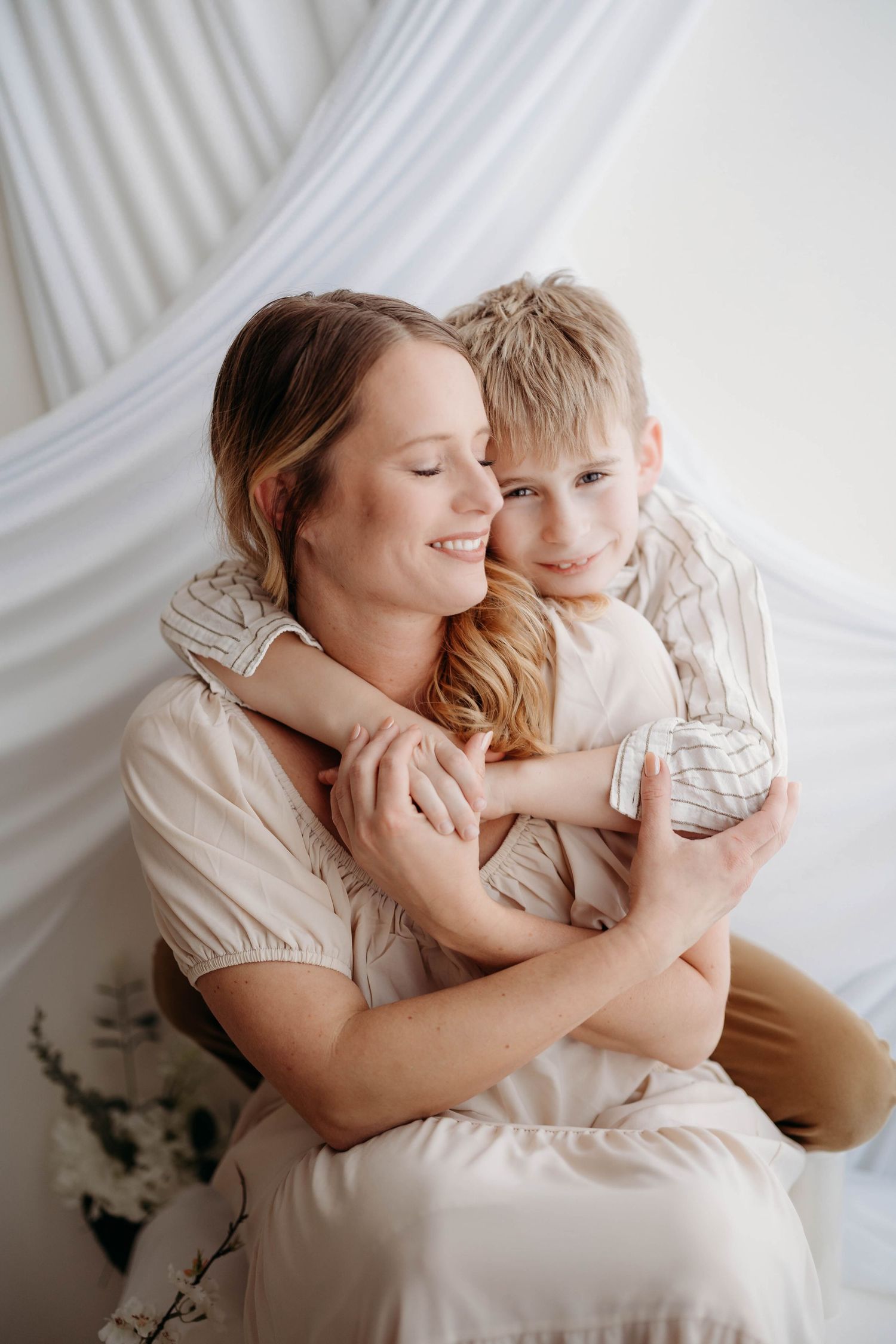 Loving mother smiling as young boy hugs her from behind in bright white studio setting. in tippecanoe county Lafayette indiana