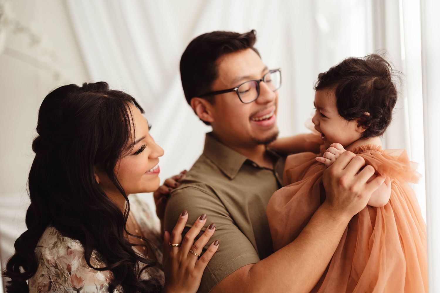 Joyful Asian family with father holding laughing baby girl in orange tulle dress in bright studio. Lafayette indiana tippecanoe county