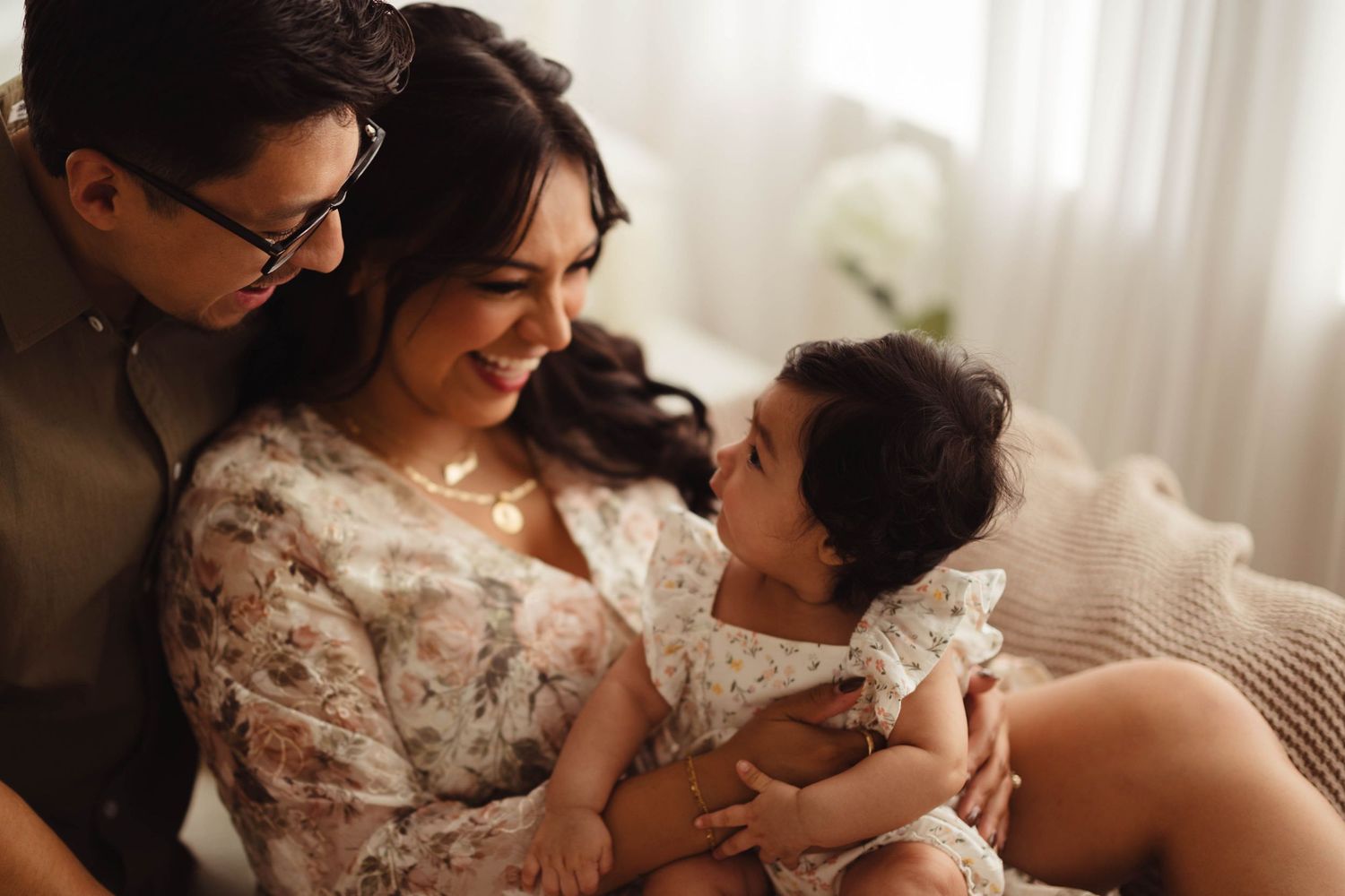 Happy family with mother in floral dress laughing with father and baby girl in bright studio setting. Lafayette indiana tippecanoe county