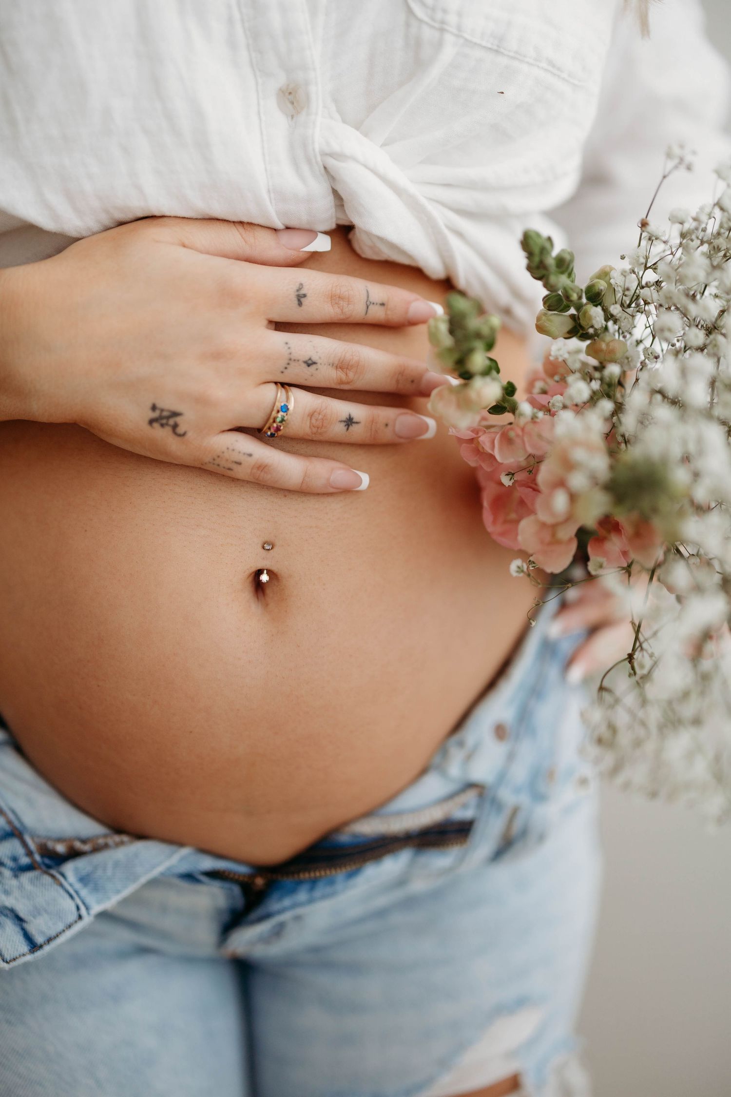 Close-up of pregnant woman in white shirt holding flowers against her tattooed belly. Lafayette indiana tippecanoe county west lafayette
