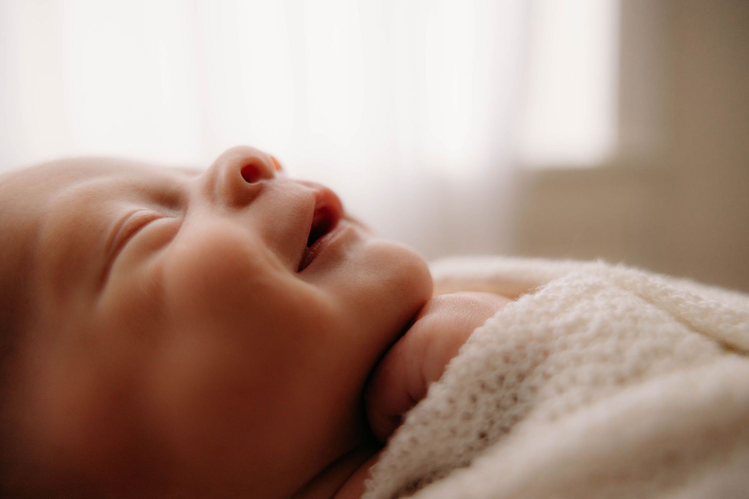 Peaceful sleeping newborn baby with slightly open mouth wrapped in soft white blanket near window. Lafayette indiana tippecanoe county