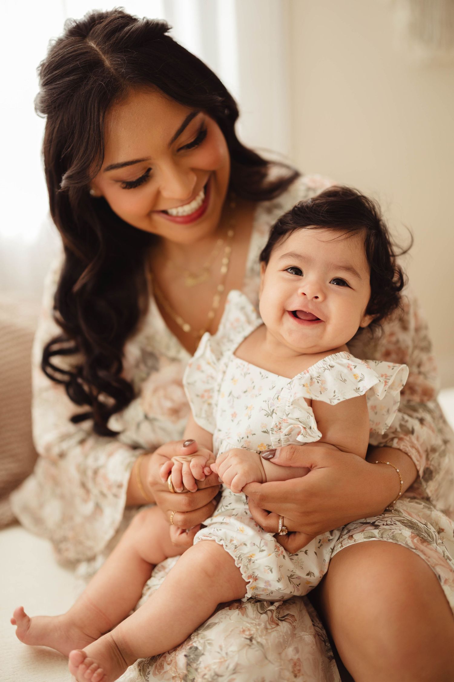 Smiling mother in floral dress holds laughing baby girl in matching outfit during professional photo session. Lafayette indiana tippecanoe